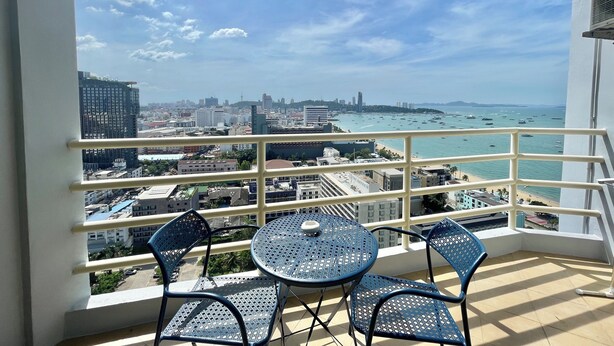 A balcony with a table and chairs, overlooking a cityscape and the sea. - Viewtalay6 by Pat 42 (Pattaya)