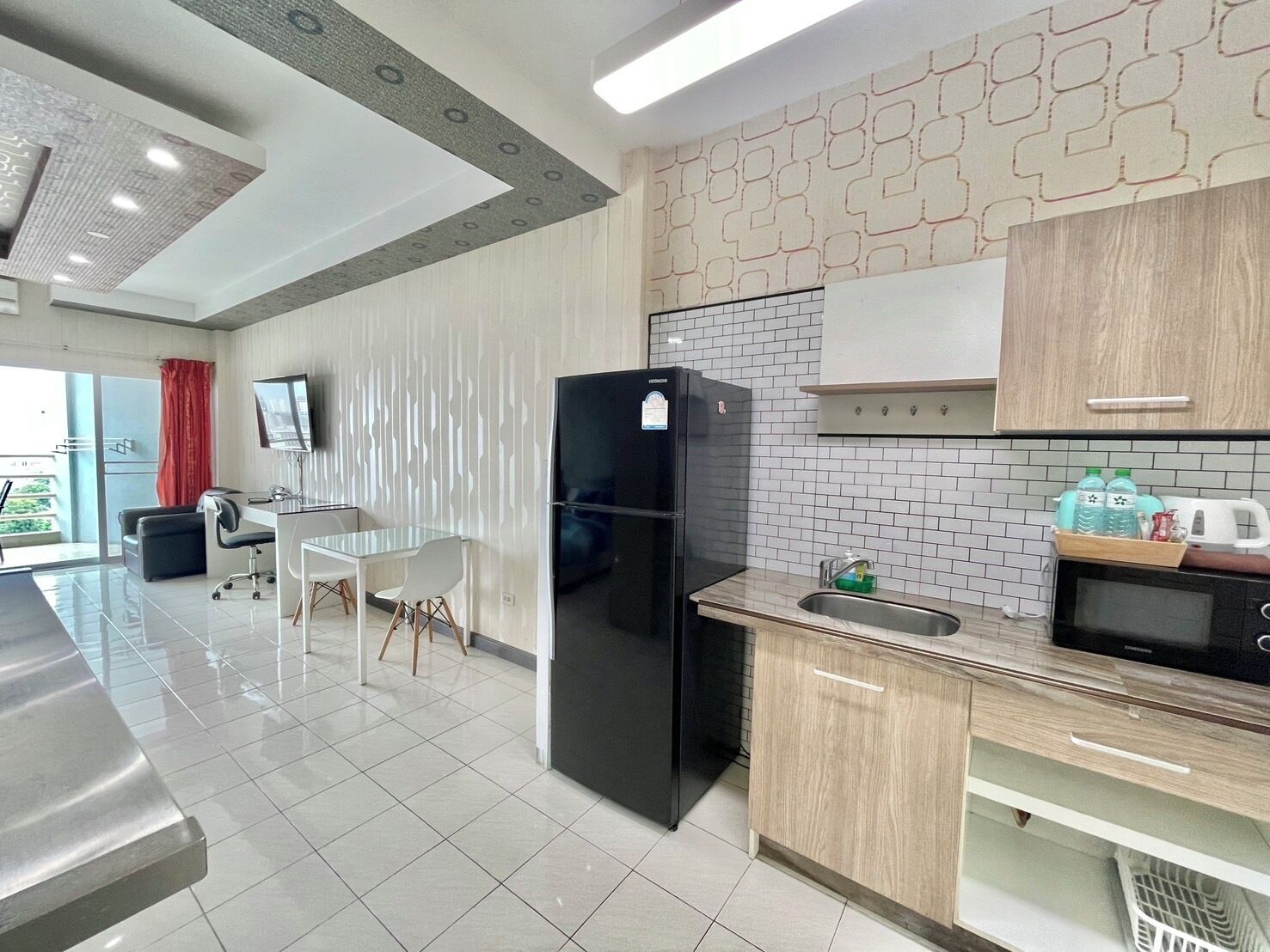 Une cuisine moderne équipée d’un réfrigérateur, d’un évier et d’un four à micro-ondes. On y trouve également un coin repas avec une table et des chaises. La cuisine est dotée d’un dosseret carrelé et de meubles de rangement en bois.