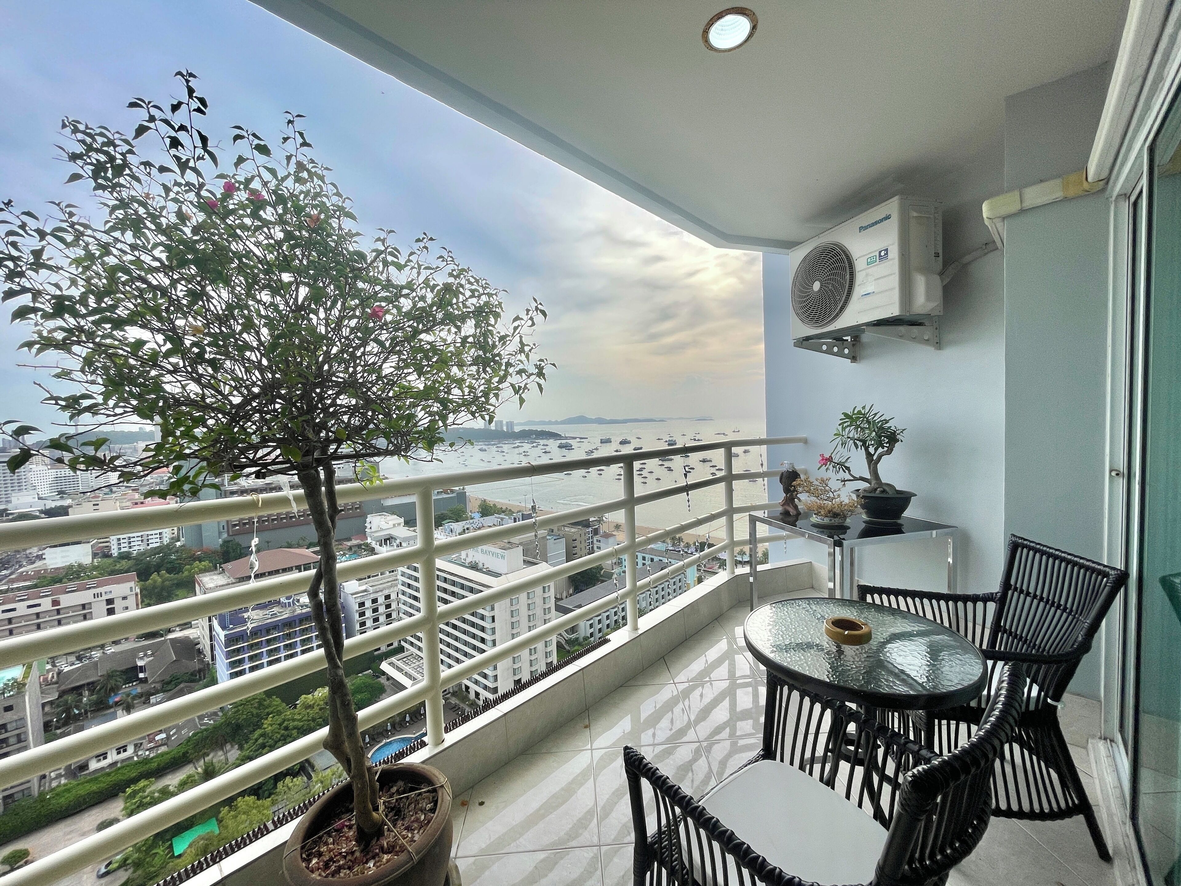 A balcony with a potted tree, a table with chairs, and a view of the cityscape and water.