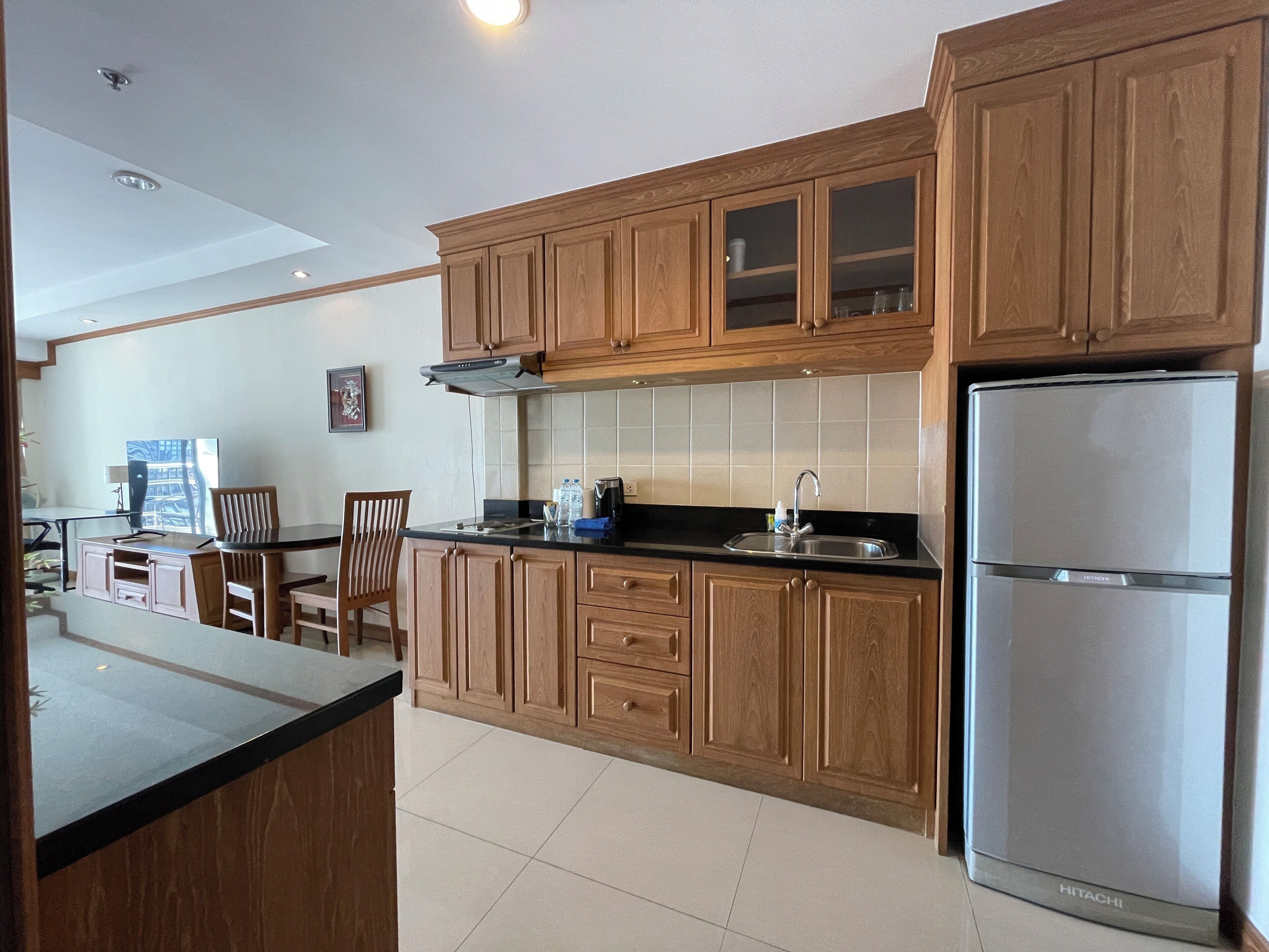 A kitchen with wooden cabinets, a stainless steel refrigerator, and a dining area with a table and chairs.