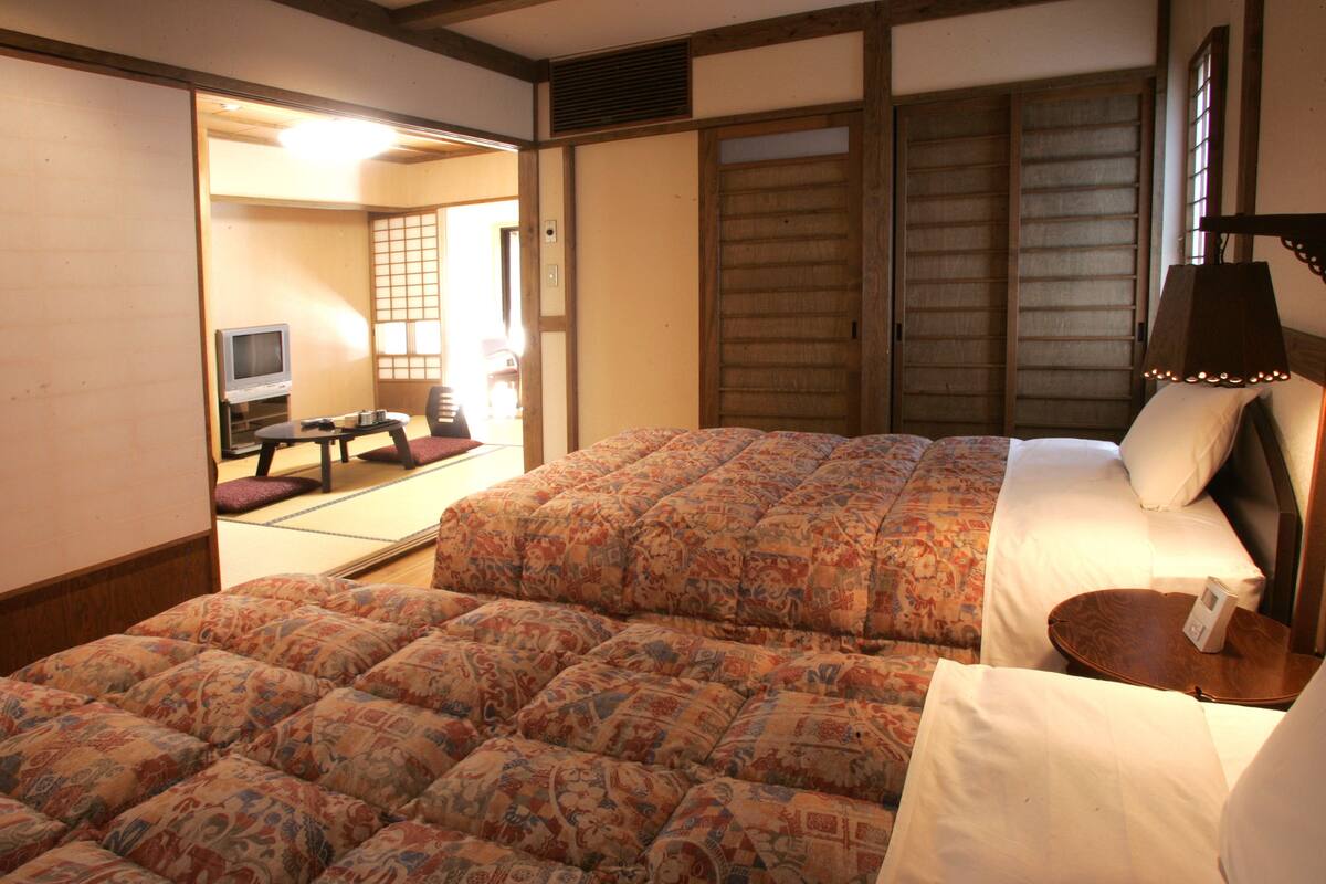 A traditional Japanese-style room with tatami flooring, a low wooden bed with a patterned bedspread, and a television in the corner.