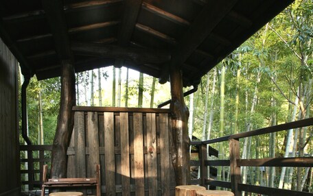 A wooden deck with a long table and several wooden stools, surrounded by a bamboo fence.