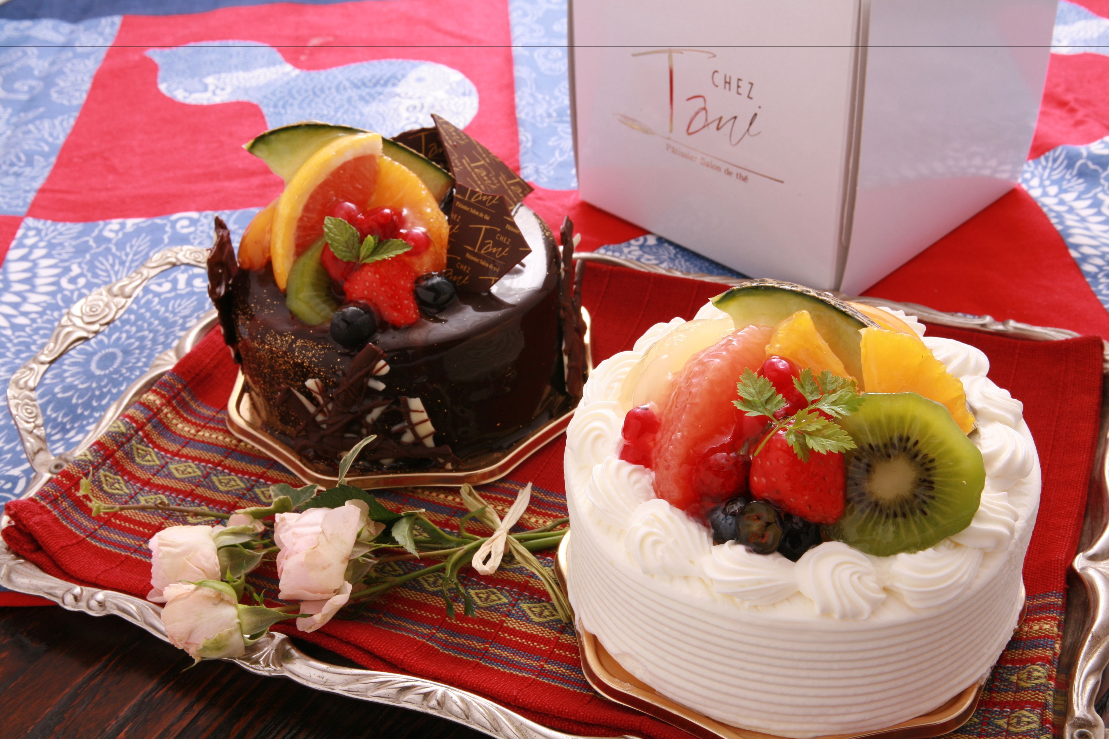 Two cakes on a table with a box labeled "Chez Tanji" in the background.