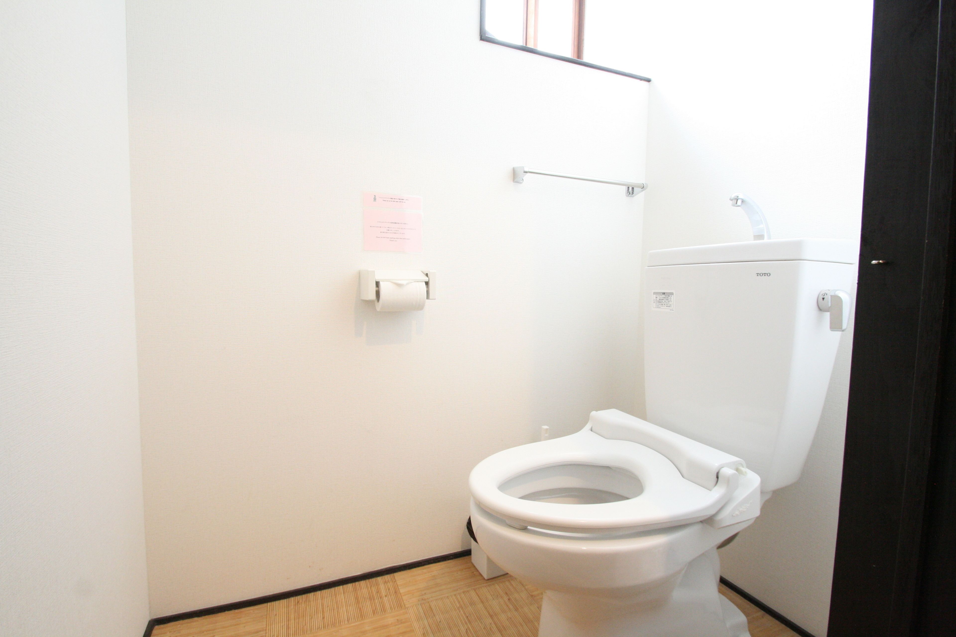 A small, clean bathroom with a white toilet, a paper towel dispenser, and a visible toilet paper roll.
