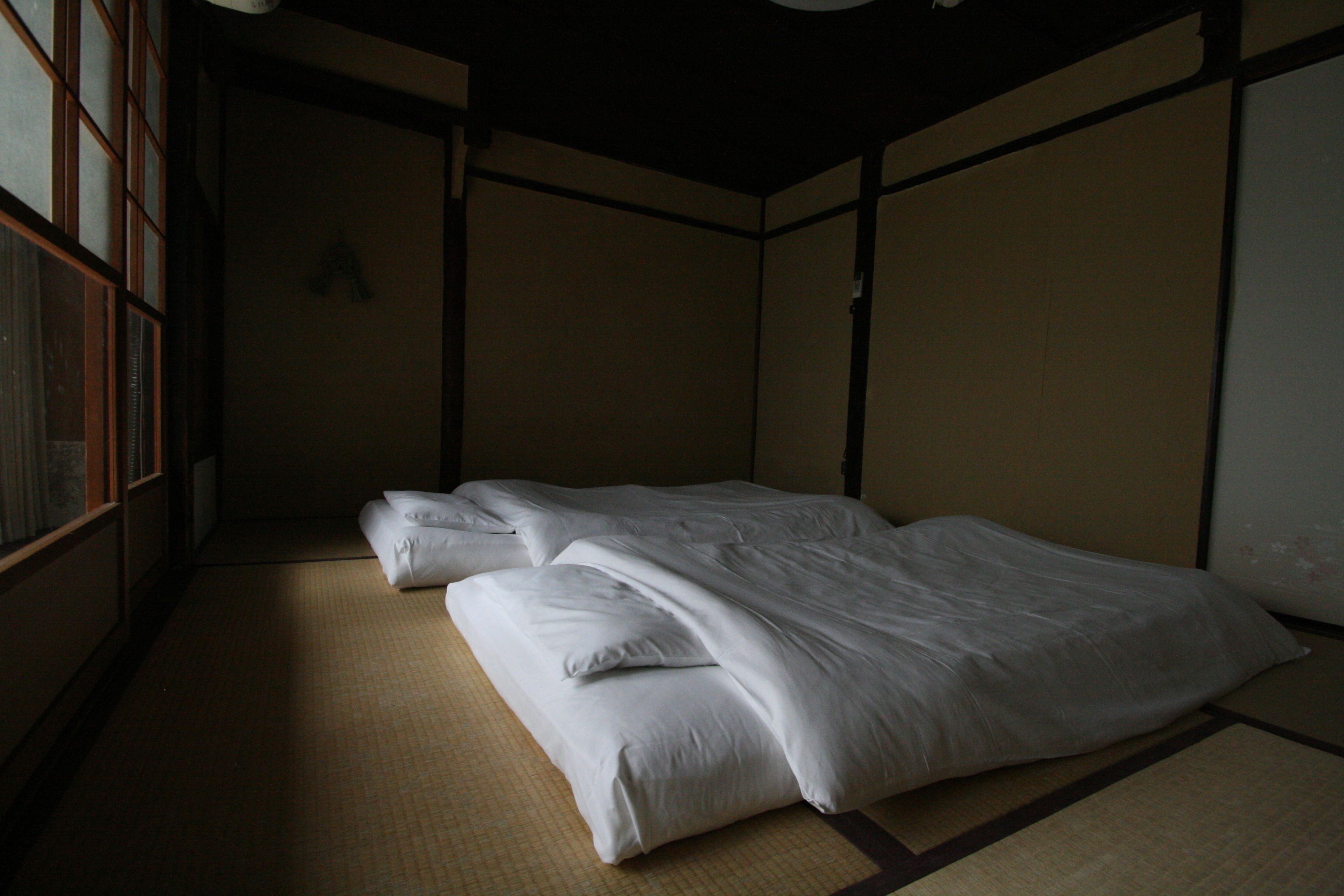 Una habitación tradicional japonesa con suelo de tatami, una cama baja con ropa blanca y puertas correderas.