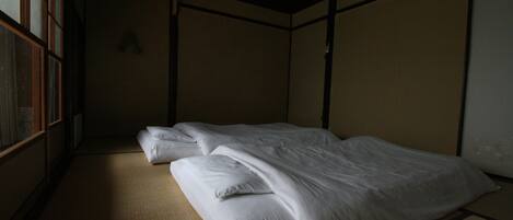 Una habitación tradicional japonesa con suelo de tatami, una cama baja con ropa blanca y puertas correderas.