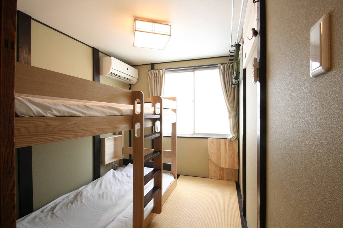 Une chambre avec un lit superposé, une fenêtre, des rideaux et un appareil de climatisation.