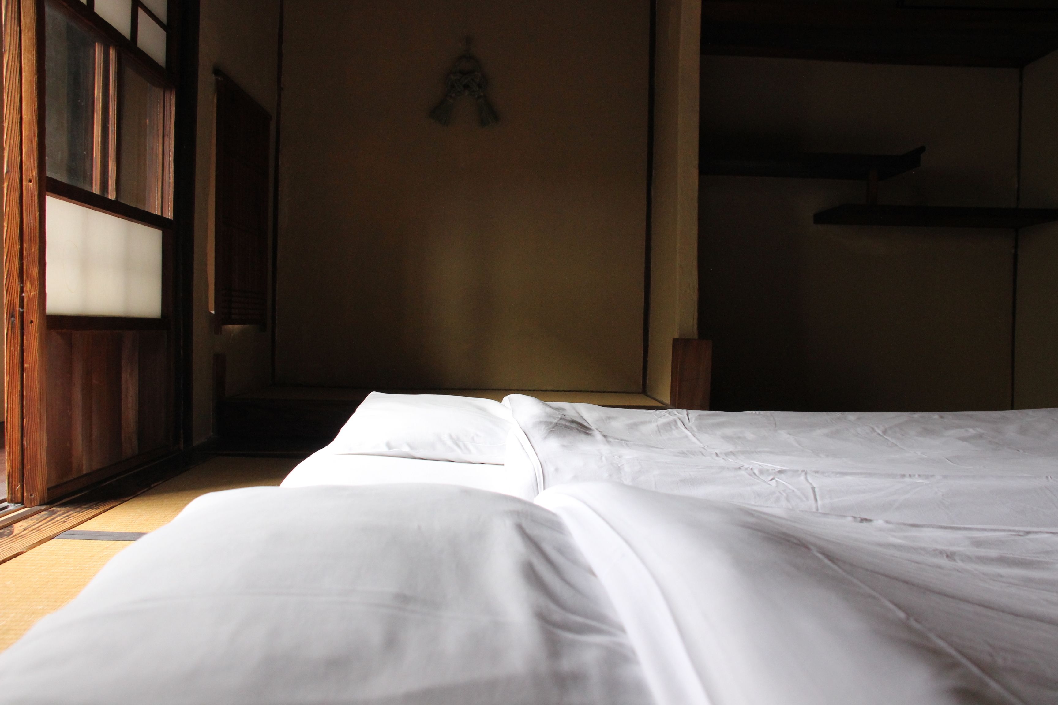 A room with a bed, wooden flooring, and a wall-mounted shelf.