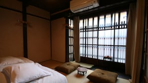 Une pièce de style japonais traditionnel, avec un sol recouvert de tatamis, un futon servant de lit, une petite table et une vue à travers des paravents en papier.