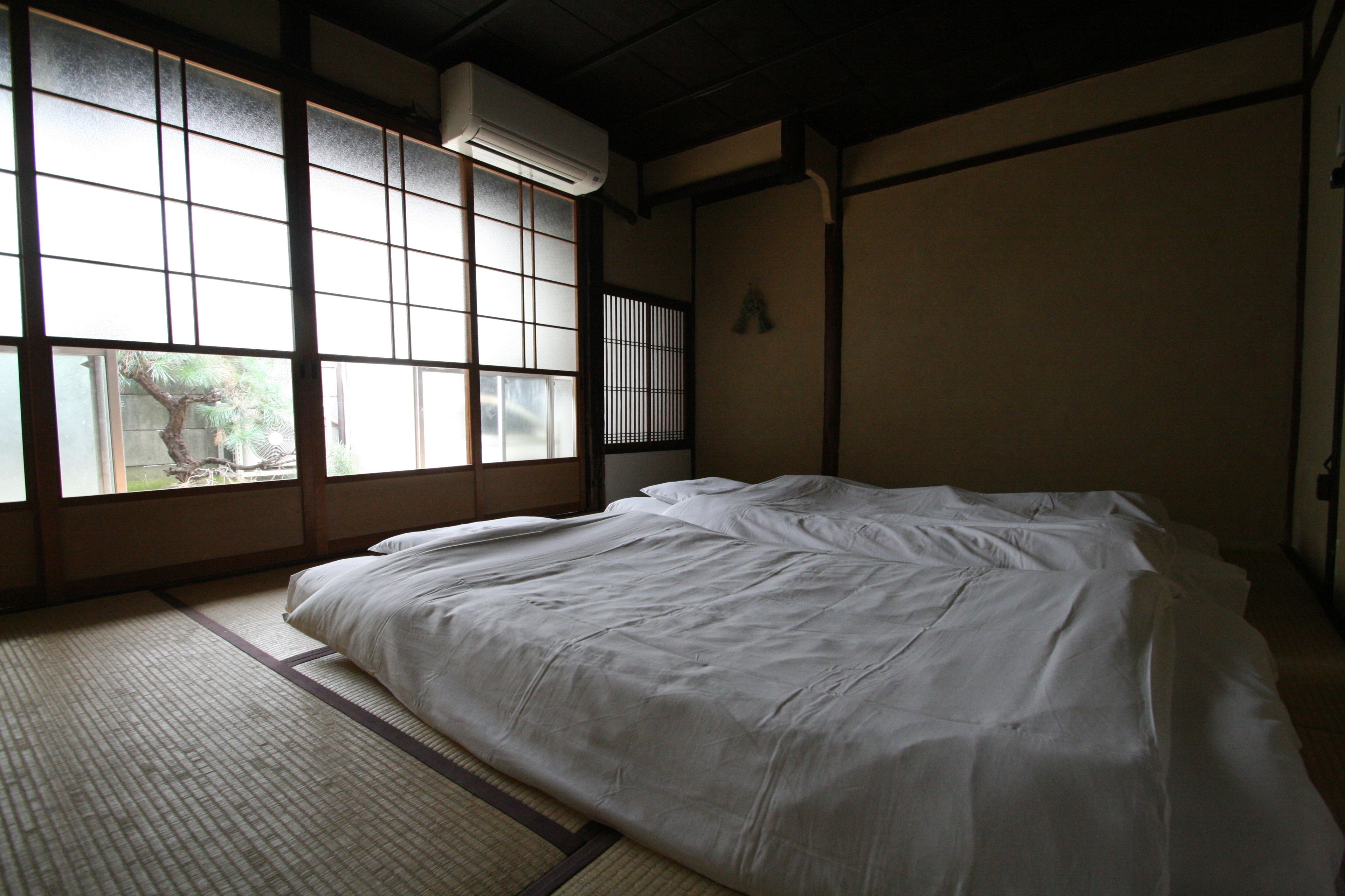 Een traditionele Japanse kamer met tatami vloerbedekking, een groot raam met shoji schermen en een bed met witte beddengoed.