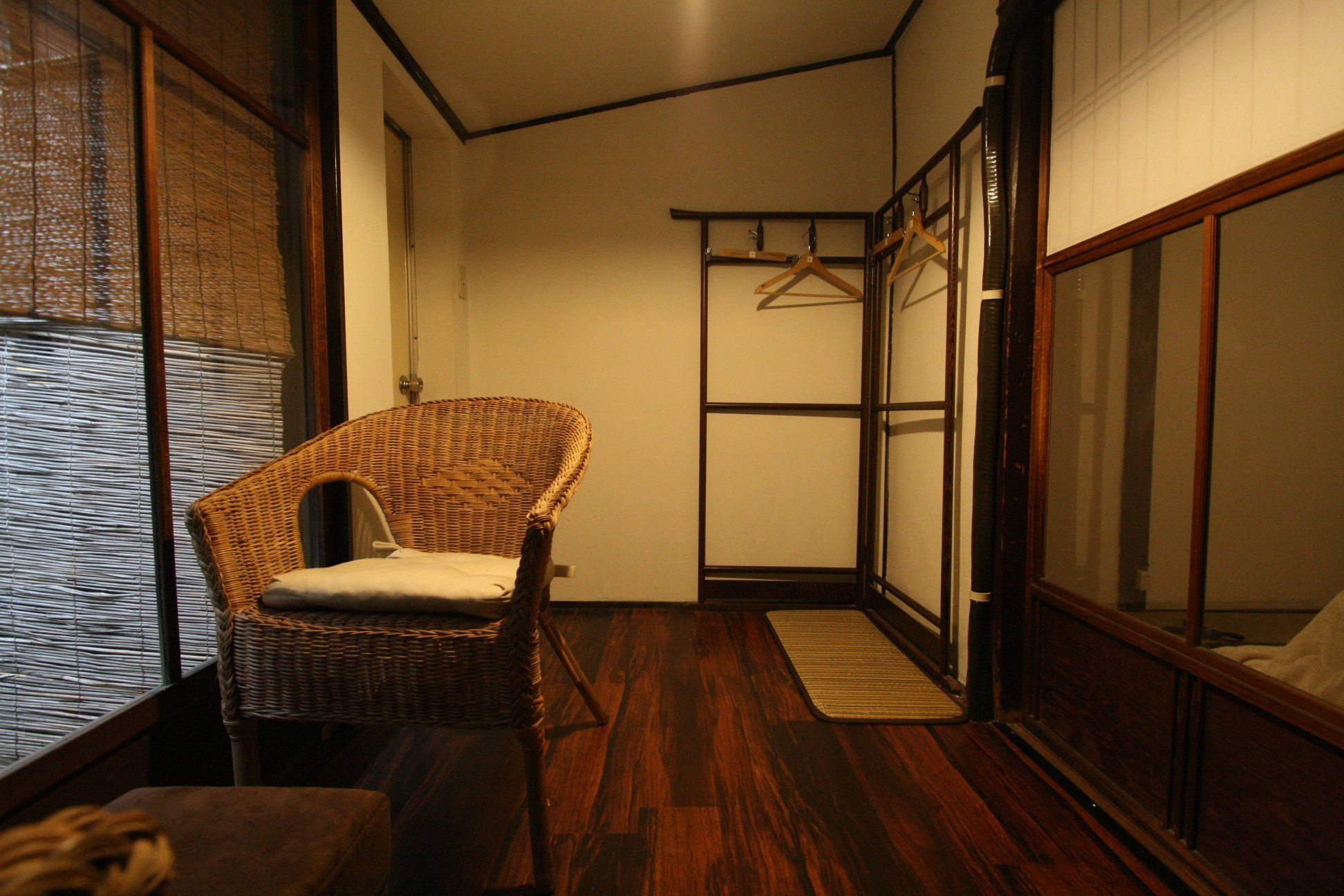 A room with a wicker chair, a wooden floor, a sliding door, and a hanging clothes rack.