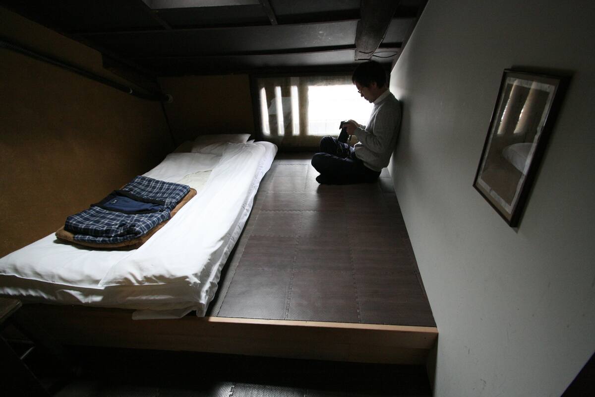 Une petite pièce faiblement éclairée, avec un lit simple, une fenêtre avec des rideaux et un tableau encadré accroché au mur.