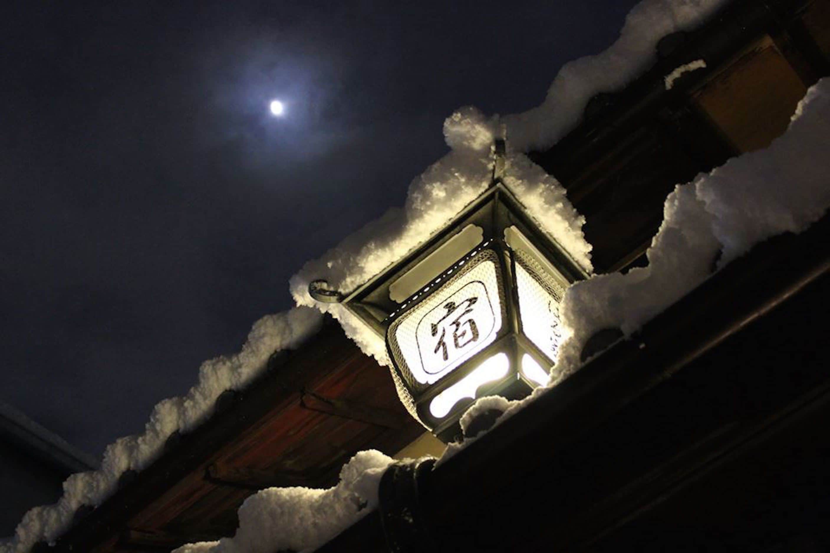 A snow-covered roof with a lit lantern displaying Chinese characters.