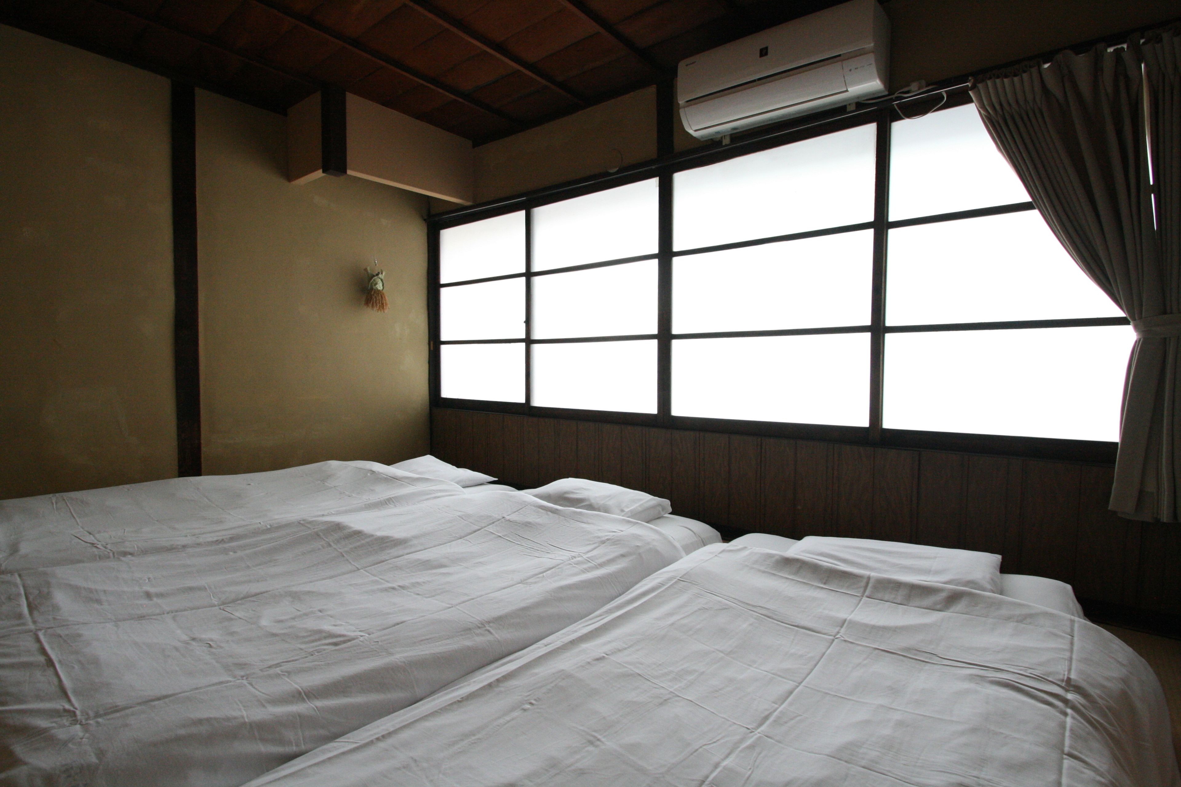 Una habitación con dos camas, una ventana con cortinas, un equipo de aire acondicionado y una lámpara fijada a la pared.