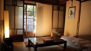 Une pièce de style japonais traditionnel, avec un sol recouvert de tatamis, une table basse, un futon servant de lit et une porte coulissante donnant sur un paysage verdoyant.