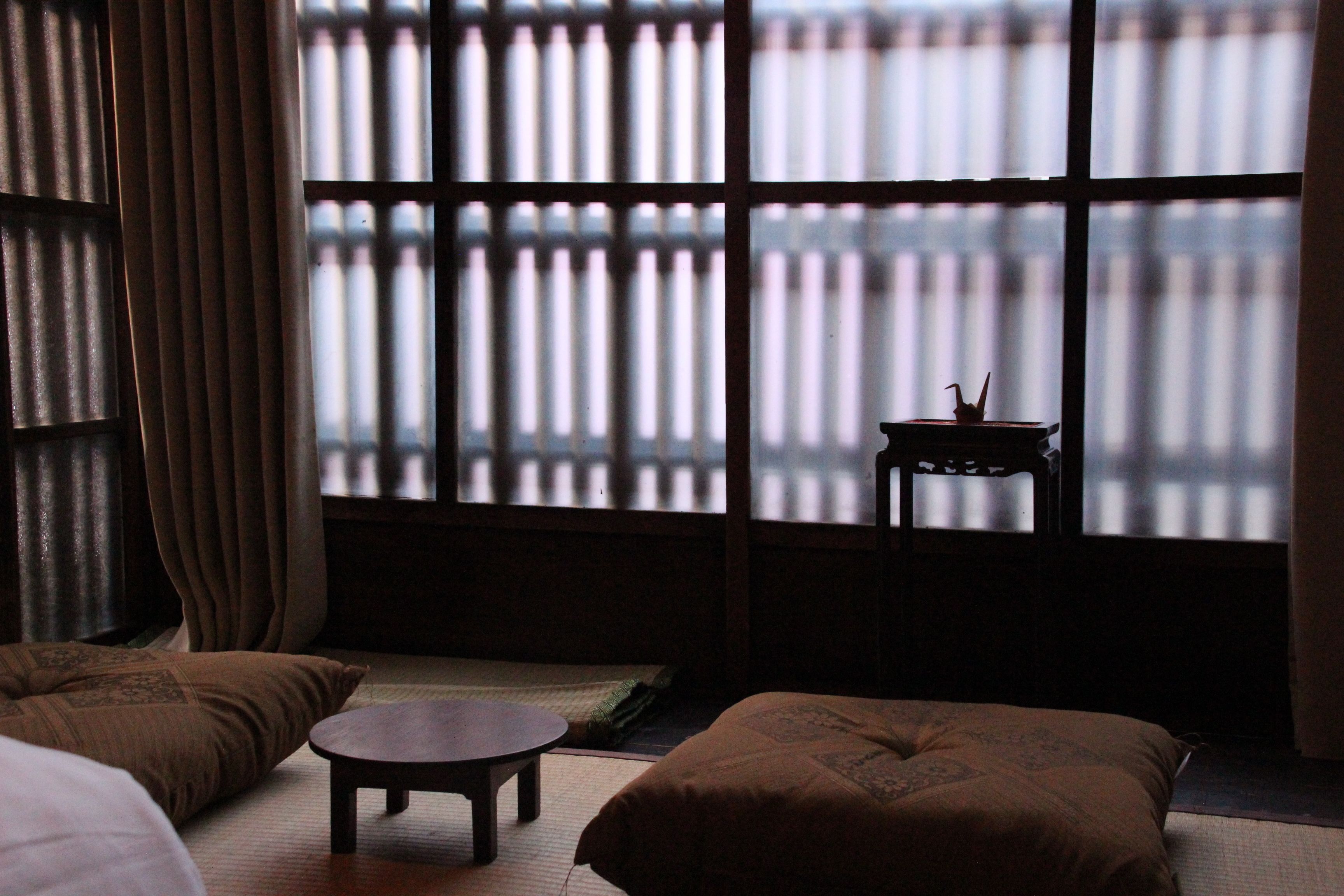 Una habitación tradicional japonesa con suelo de tatami, una mesa baja, cojines y vistas a través de biombos shoji.