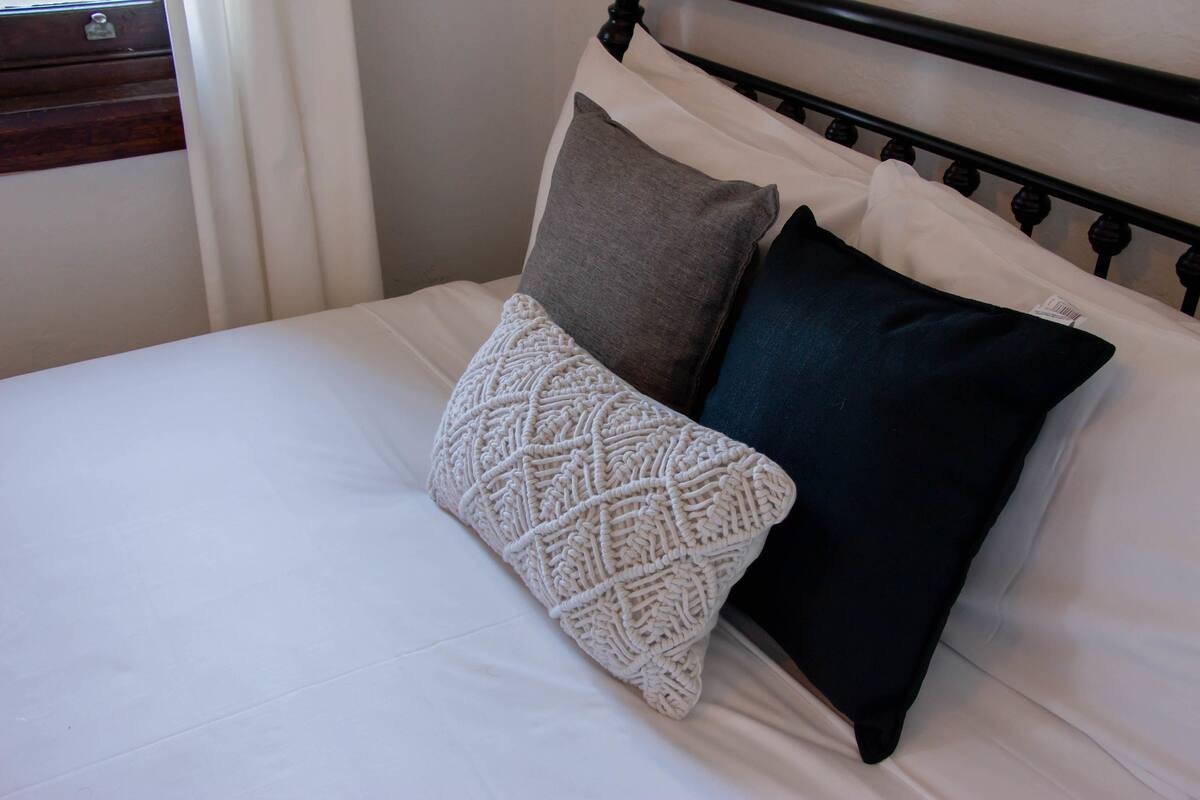 A bed with a white sheet, a grey pillow, and a black pillow.