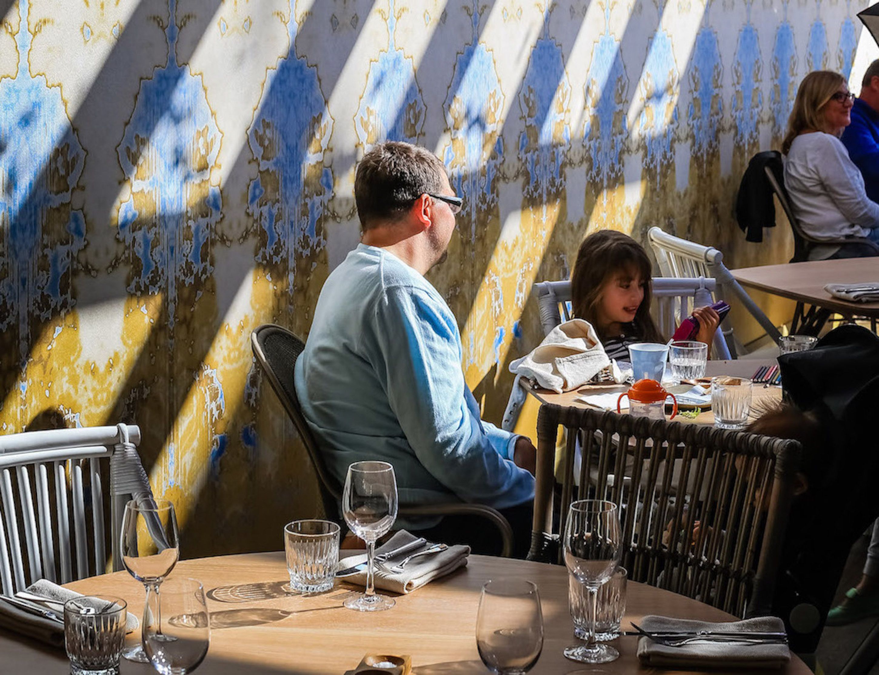 A restaurant with outdoor seating, tables with chairs, and a decorative wall with a blue and gold pattern.