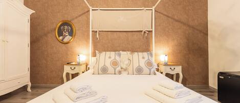 A hotel room with a bed, two bedside tables, a wardrobe, a framed picture on the wall, and a canopy bed.