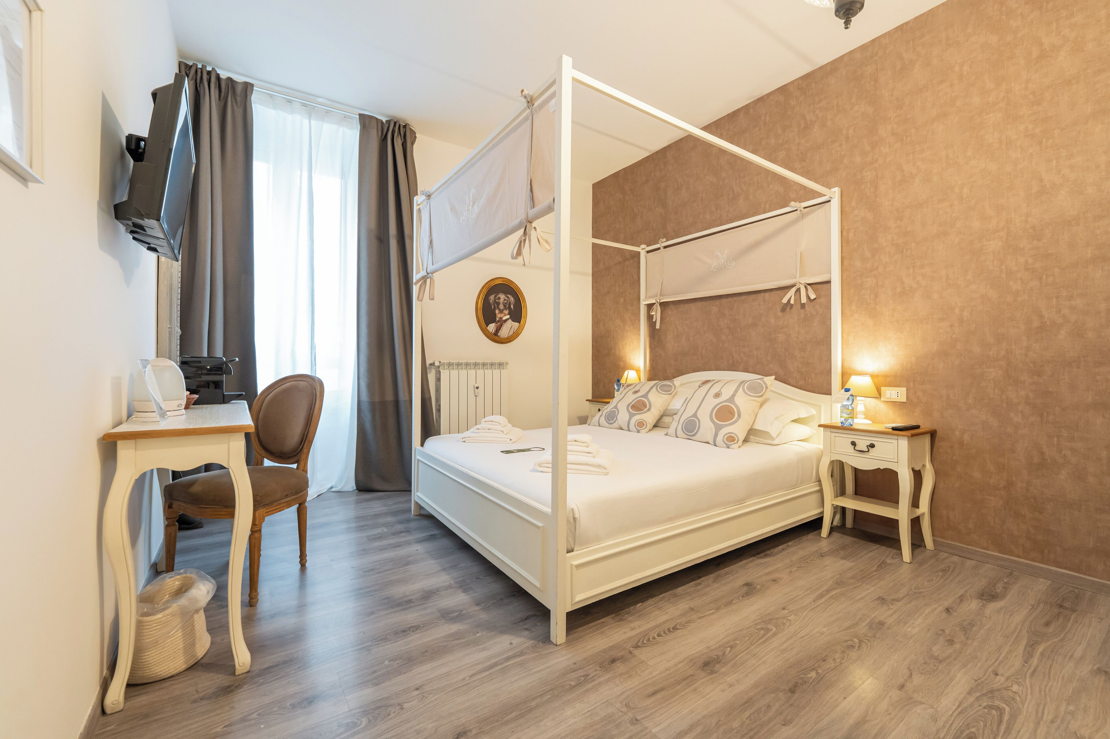 En seng med baldakin, et skrivebord med stol, et sengebord med lampe og et billedramme på væggen.