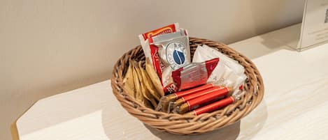 Una cesta de mimbre con varios objetos, incluyendo un paquete rojo y blanco, una bolsa de plástico transparente y algunos objetos cilíndricos rojos.