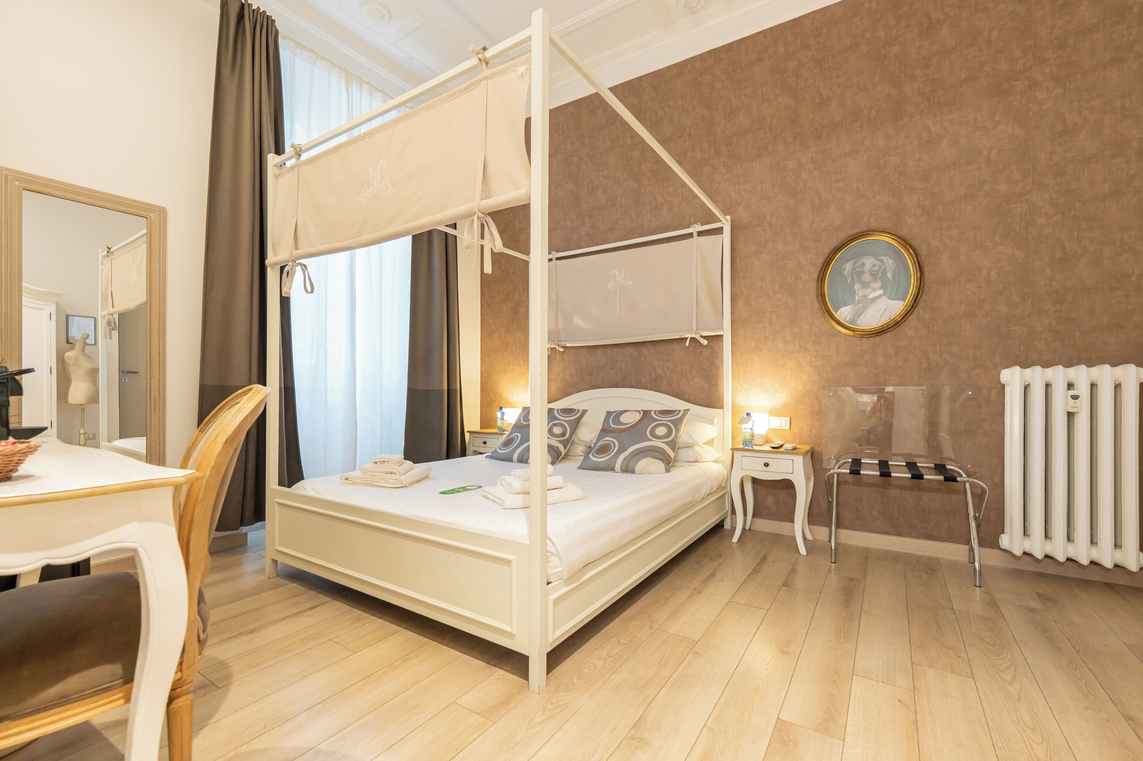 A four-poster bed with a canopy, a bedside table with a lamp, a round mirror, and a radiator.