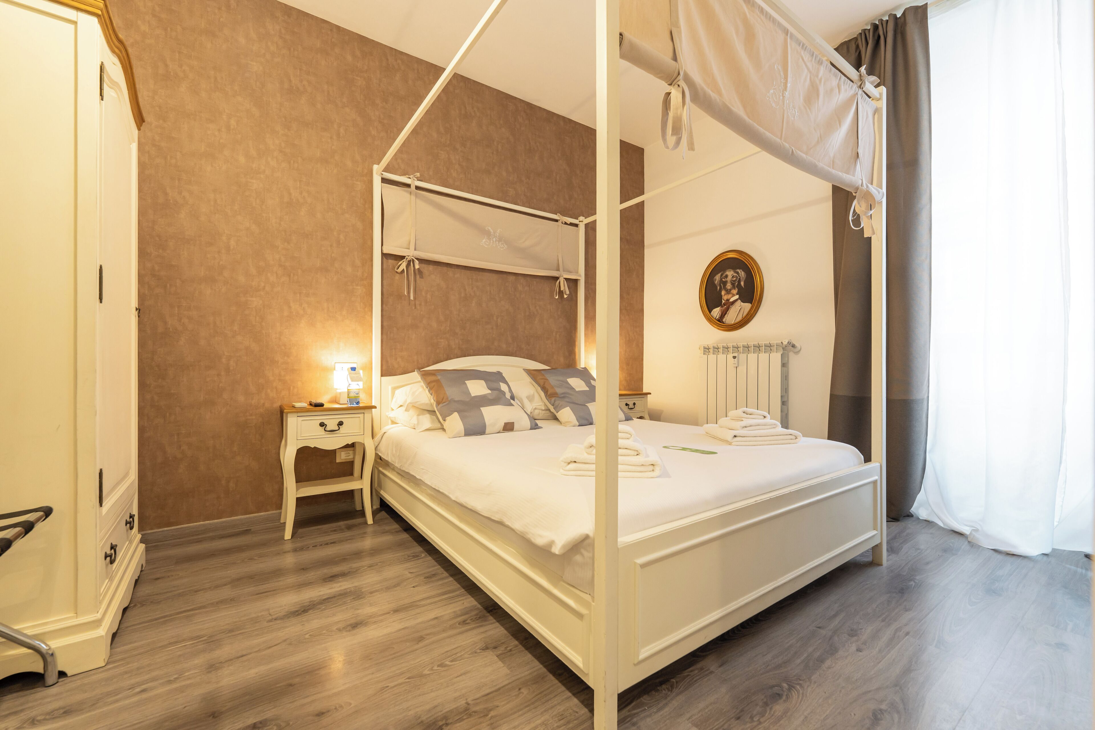 Een hemelbed, een nachtkastje met een lamp en een radiator aan de muur.