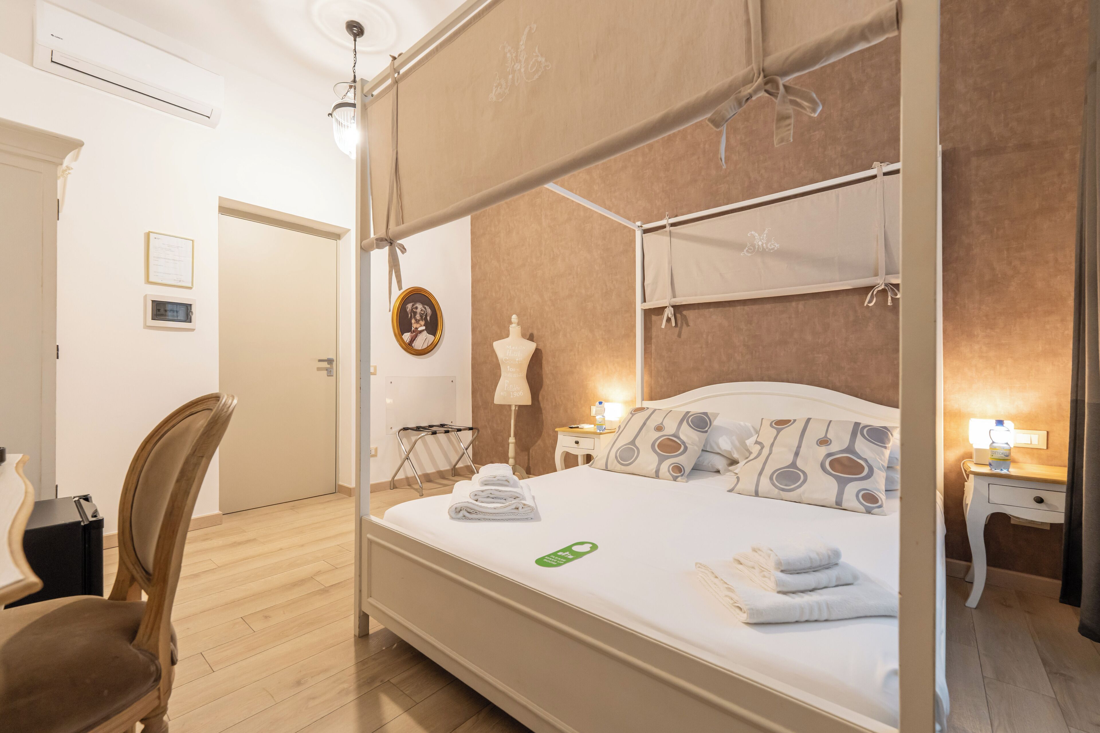 A four-poster bed with a canopy, a wooden chair, a bedside table with a lamp, and a framed picture on the wall.
