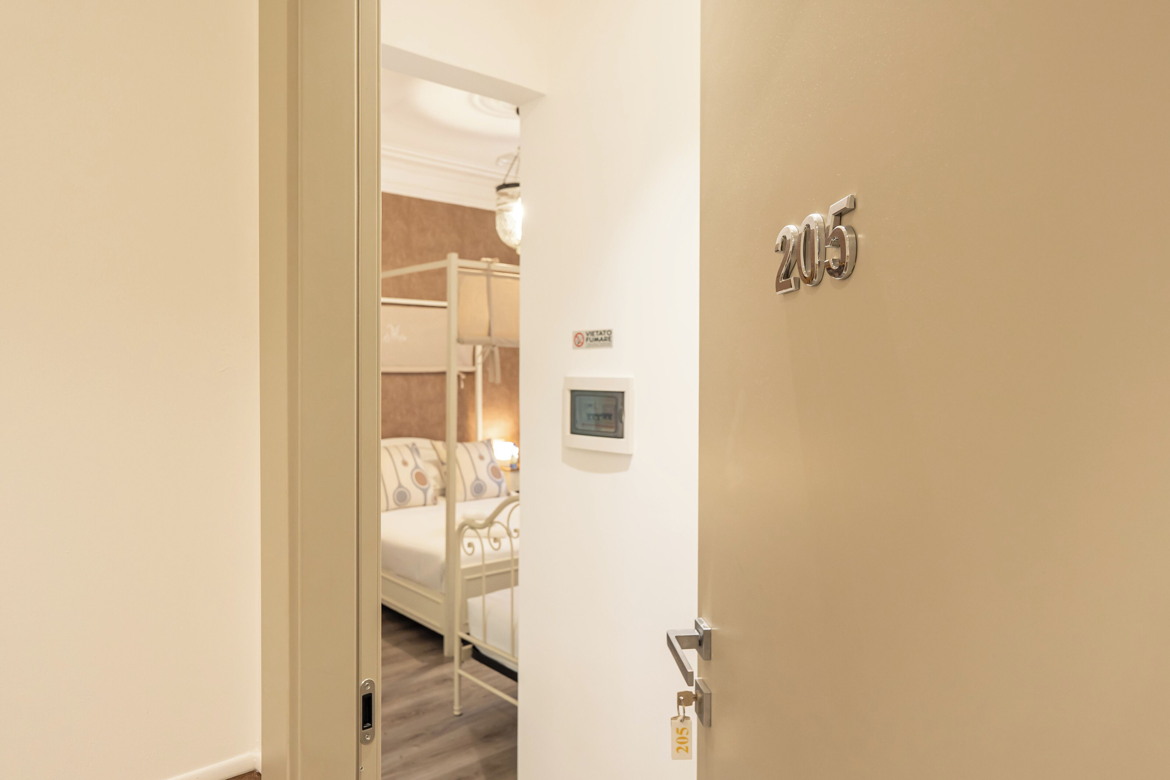 A hotel room with a bed, a bedside table, a lamp, and a door with the number 205.