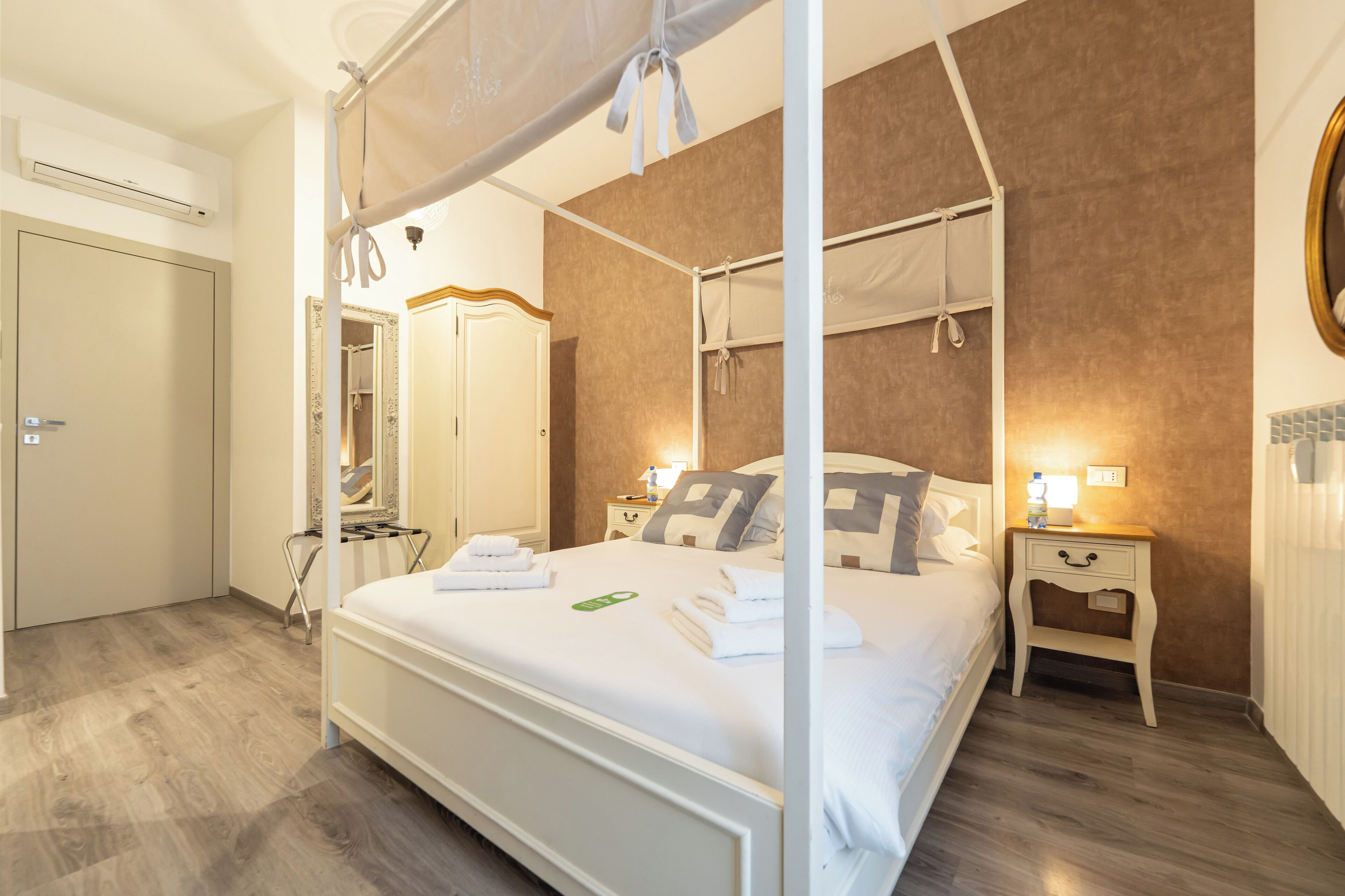 Un lit à baldaquin, une table de chevet avec une lampe et un miroir au mur.