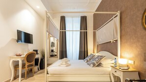 A four-poster bed with a flat-screen TV mounted on the wall, a desk with a chair, and a bedside table with a lamp. - Flaminia Rooms&Suites (Rome)