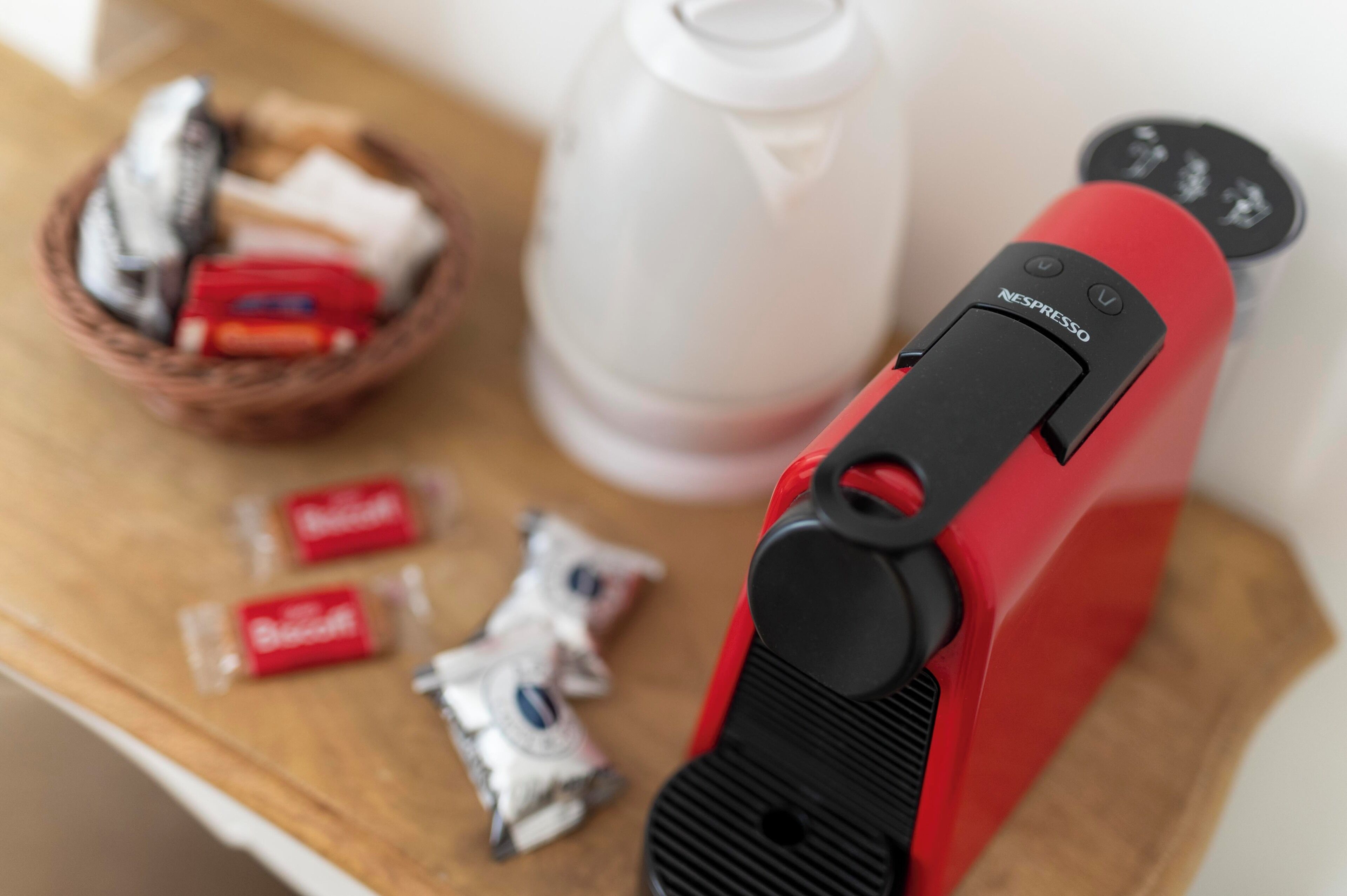 Una m áquina Nespresso roja sobre una superficie de madera, con una cesta de aperitivos y un recipiente blanco al fondo.