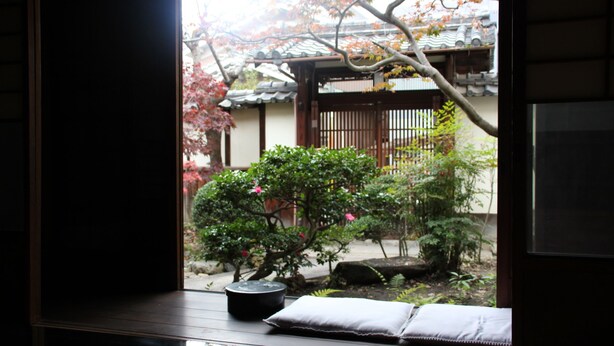 A traditional Japanese room with tatami flooring, a shoji screen, and a view of a garden with a wooden gate and cherry blossoms. - HARUYA Naramachi - Hostel (Nara)