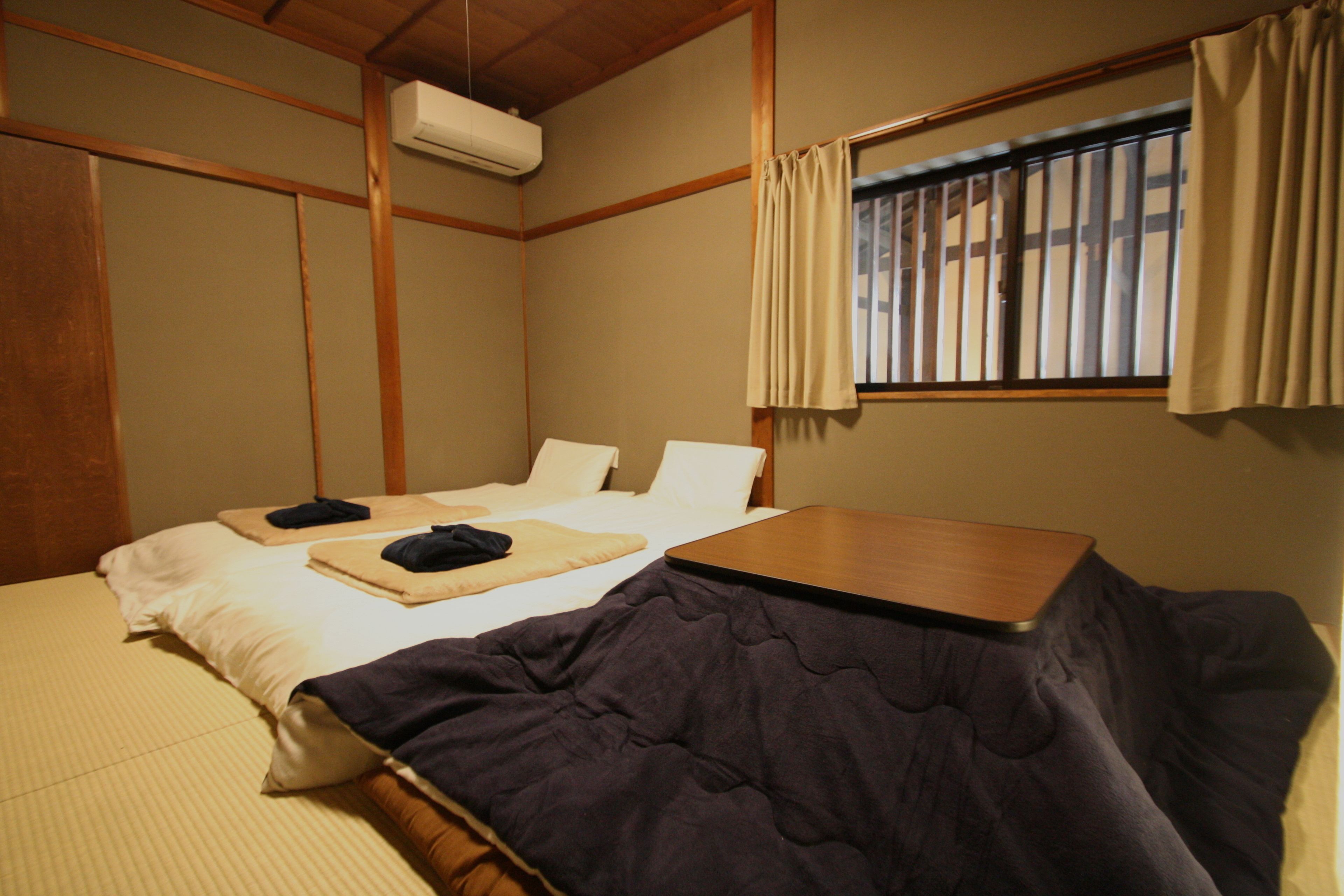 A hotel room with two beds, a wooden table, and a window with curtains.