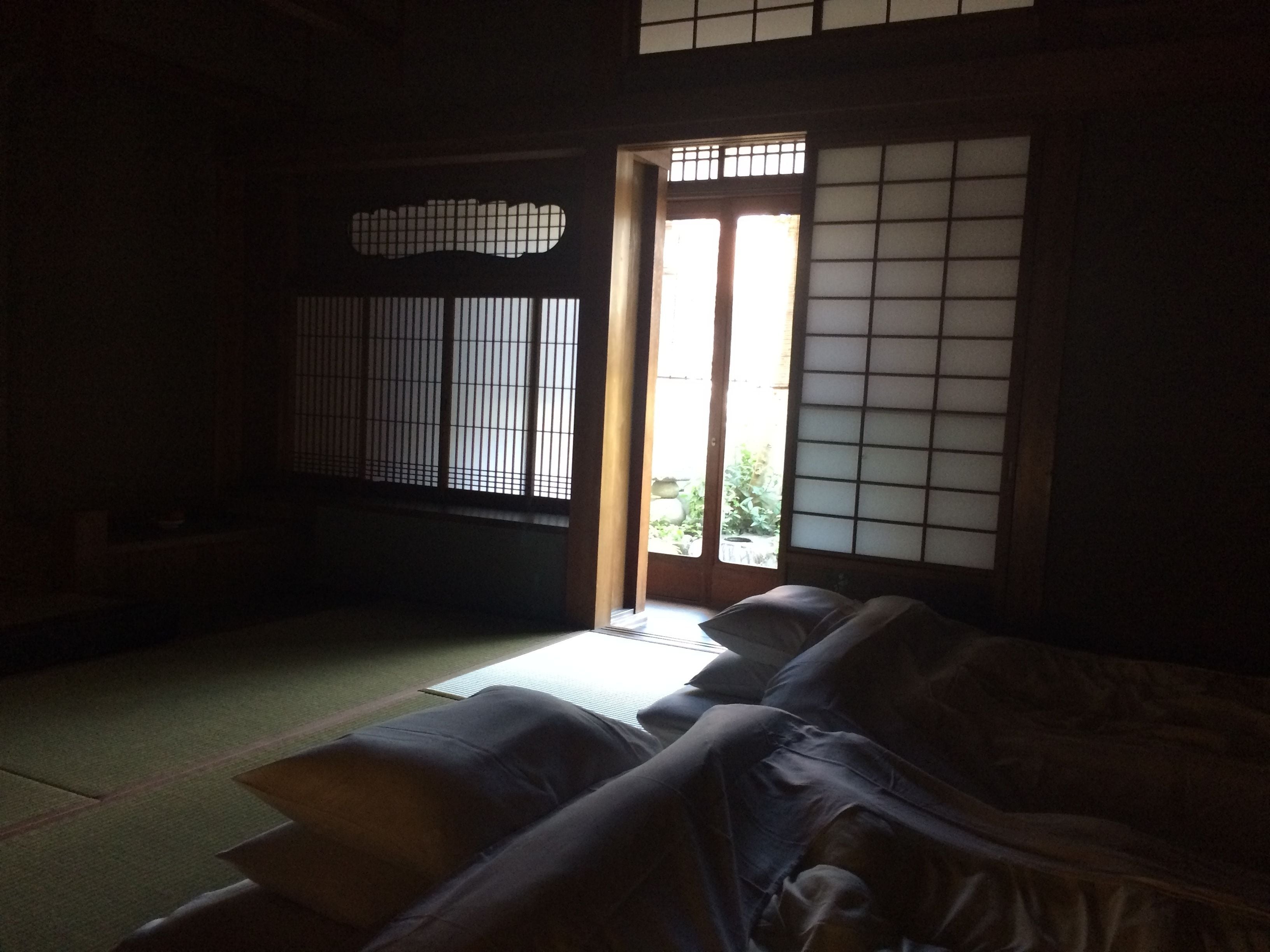 Una habitación japonesa tradicional con suelo de tatami, una mesa baja y un fusuma que da a zonas verdes exteriores.
