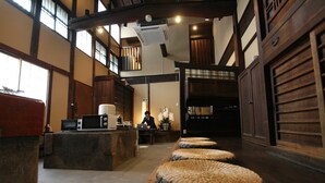 A traditional Japanese-style interior with tatami mats, a wooden reception desk, and a person working at a laptop. - HARUYA Naramachi - Hostel (Nara)