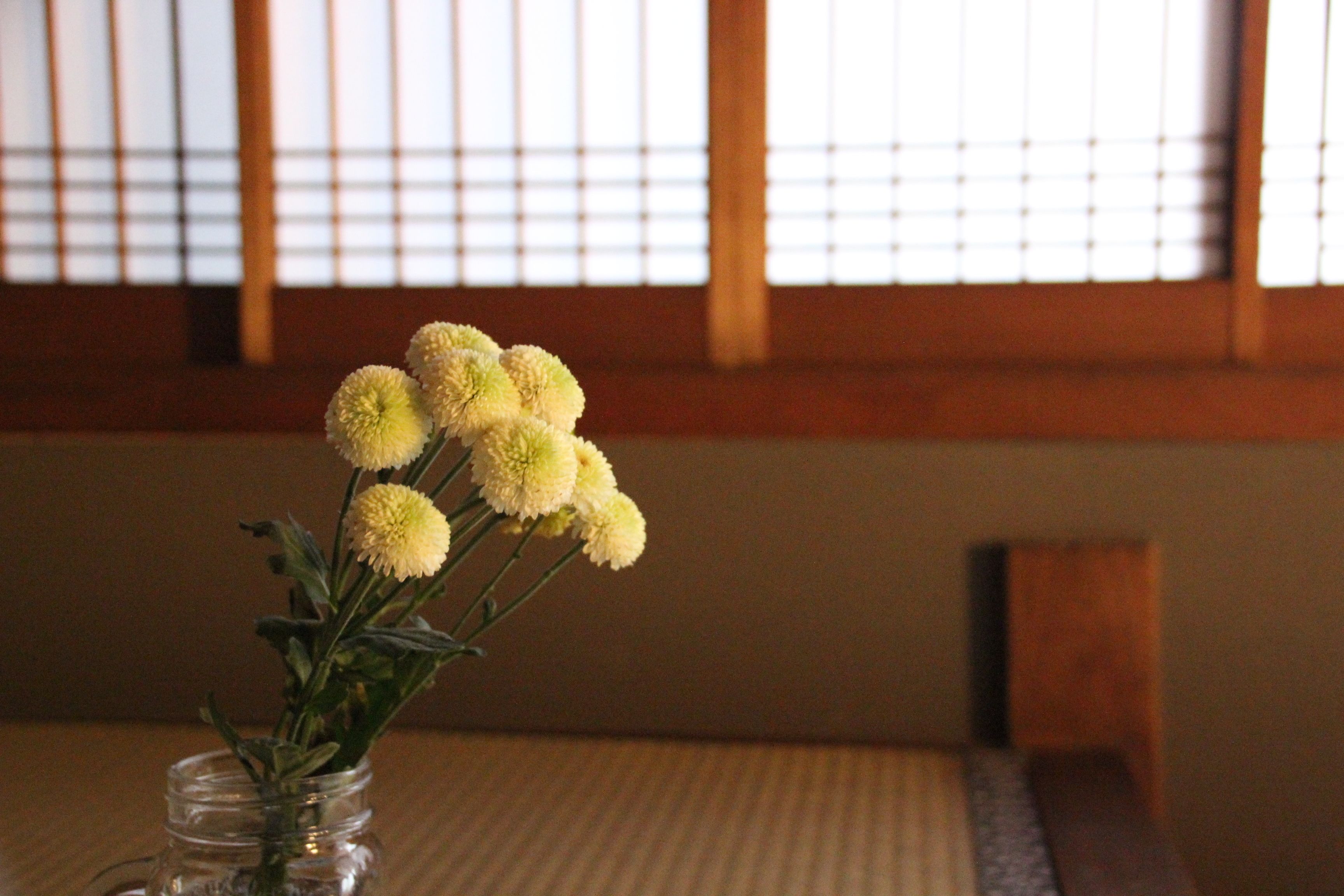 Eine Vase mit gelben Blumen auf einem Tisch in einem Raum mit Holzbalken und Tatami-Boden.