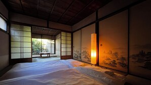 A traditional Japanese-style room with tatami flooring, a low wooden ceiling, sliding shoji doors, and a bed with white bedding. - HARUYA Naramachi - Hostel (Nara)