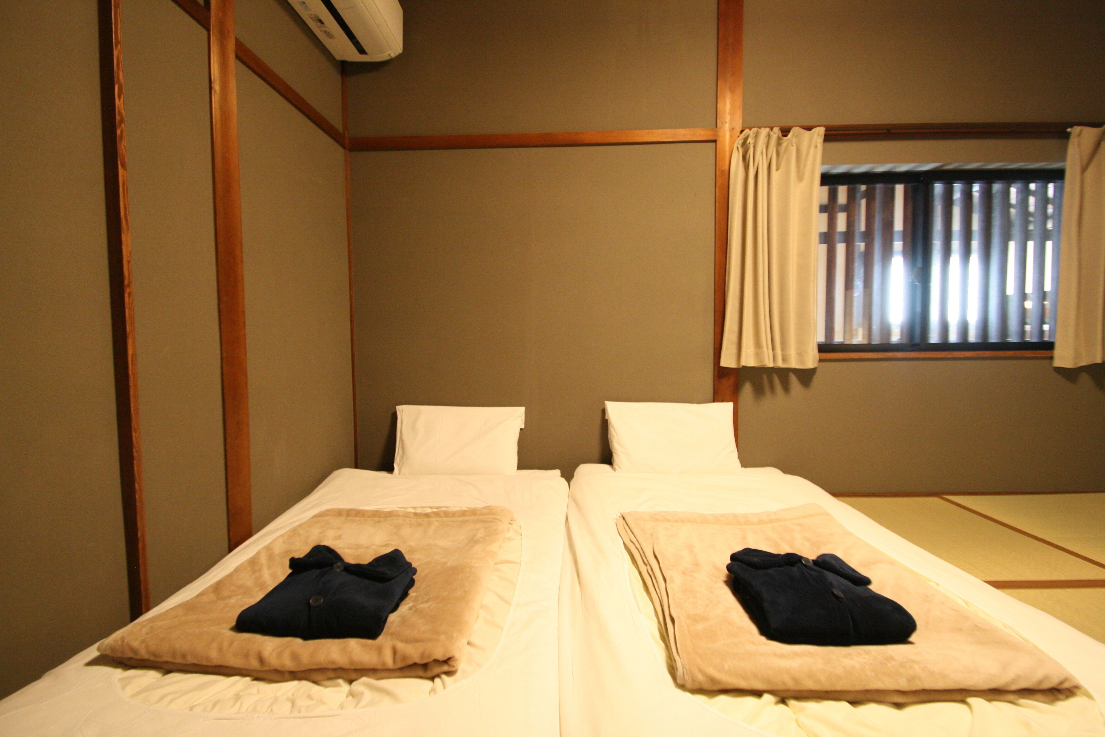 A hotel room with two single beds, a window with curtains, and a wooden wall paneling.