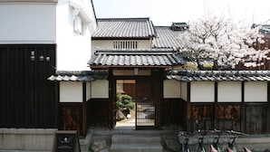 A traditional Japanese building with a tiled roof, a wooden gate, and cherry blossoms. - HARUYA Naramachi - Hostel (Nara)