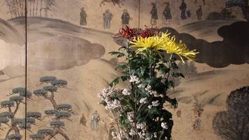 A traditional painting with figures and horses, a yellow flower, and white blossoms.