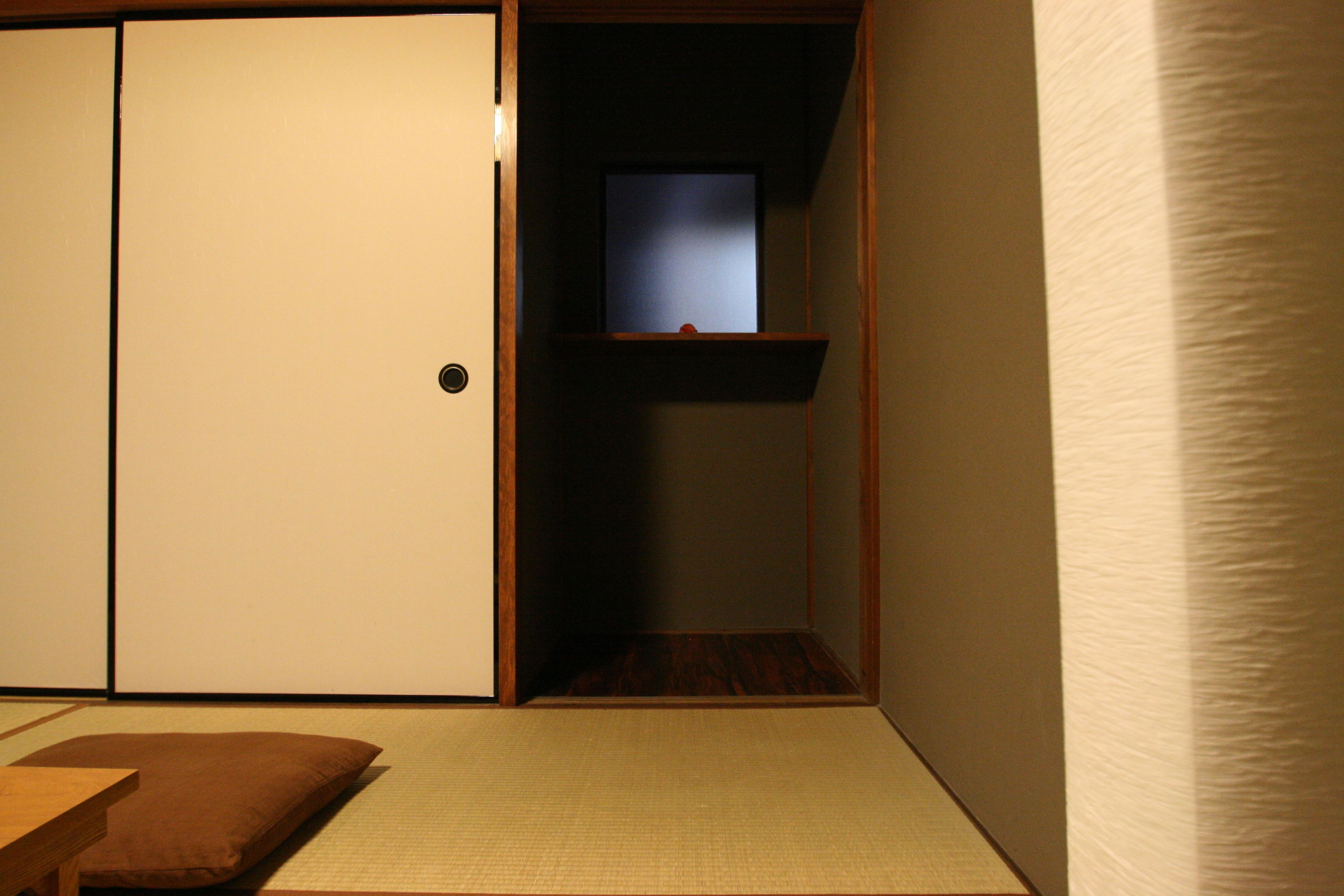 A traditional Japanese room with tatami flooring, a sliding door, a small shelf, and a window.