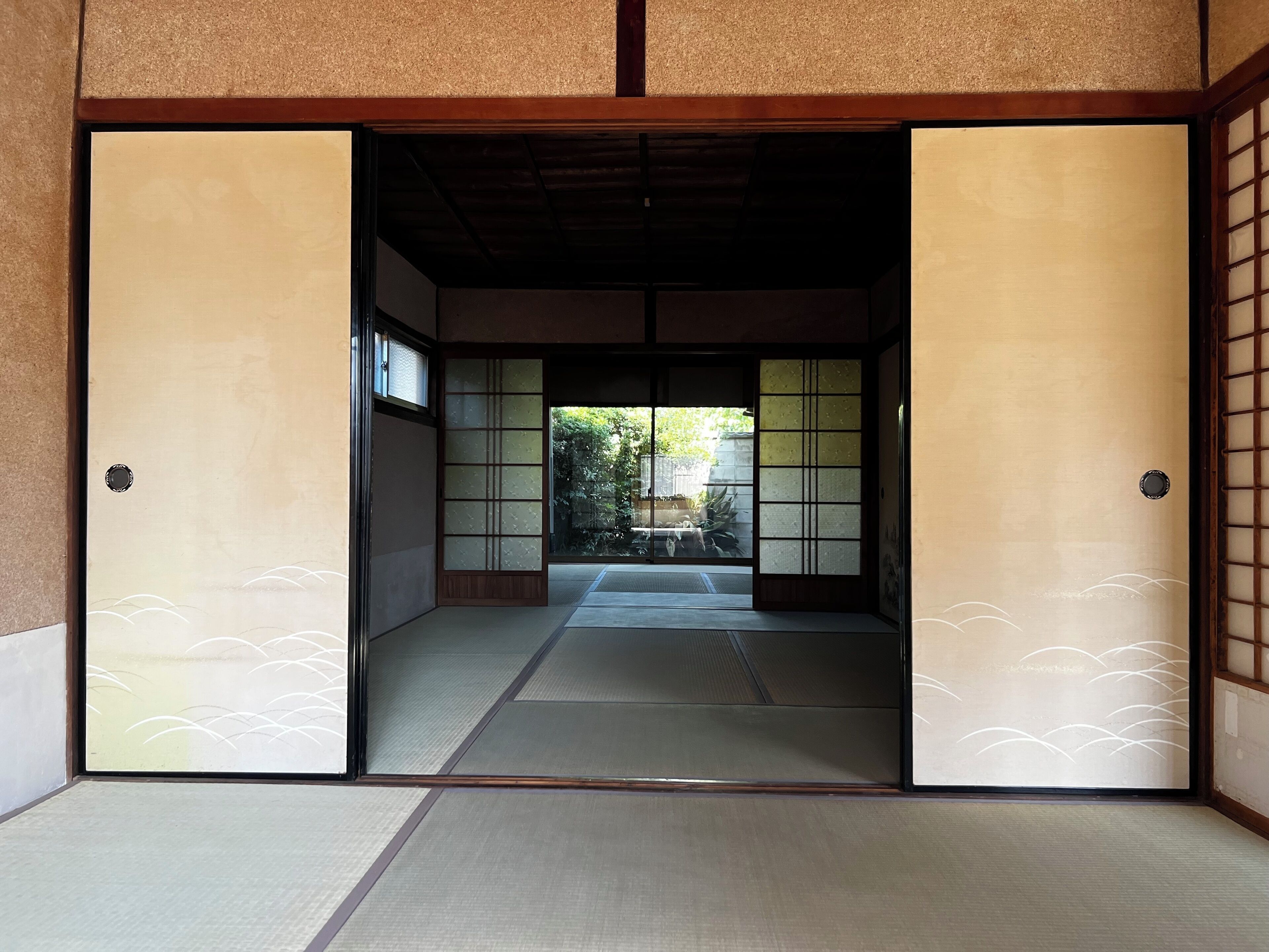 Una habitación tradicional japonesa con suelo de tatami, puertas correderas y vistas a un jardín.