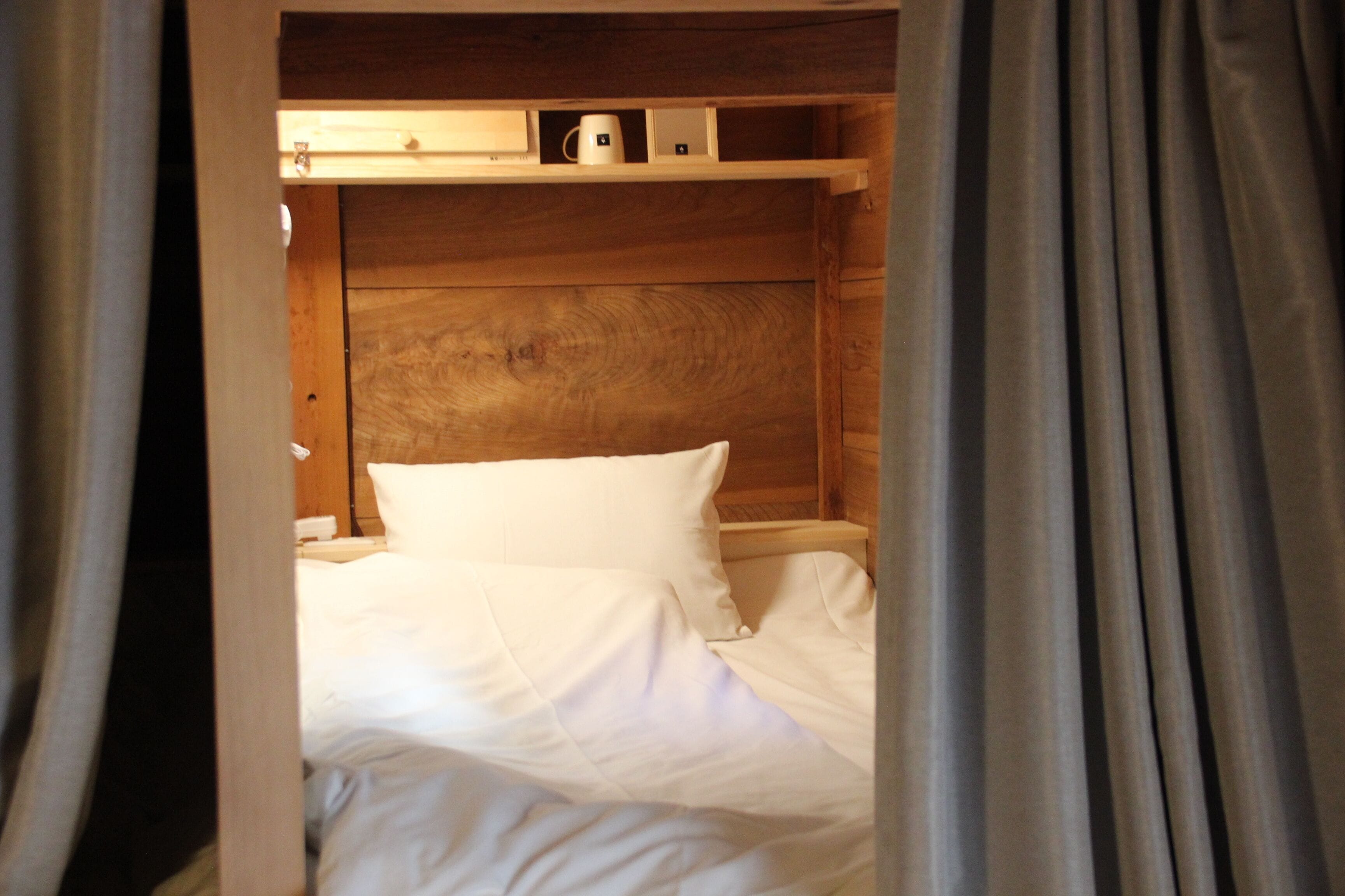A wooden bed with white linens, a nightstand, and a shelf above the bed.