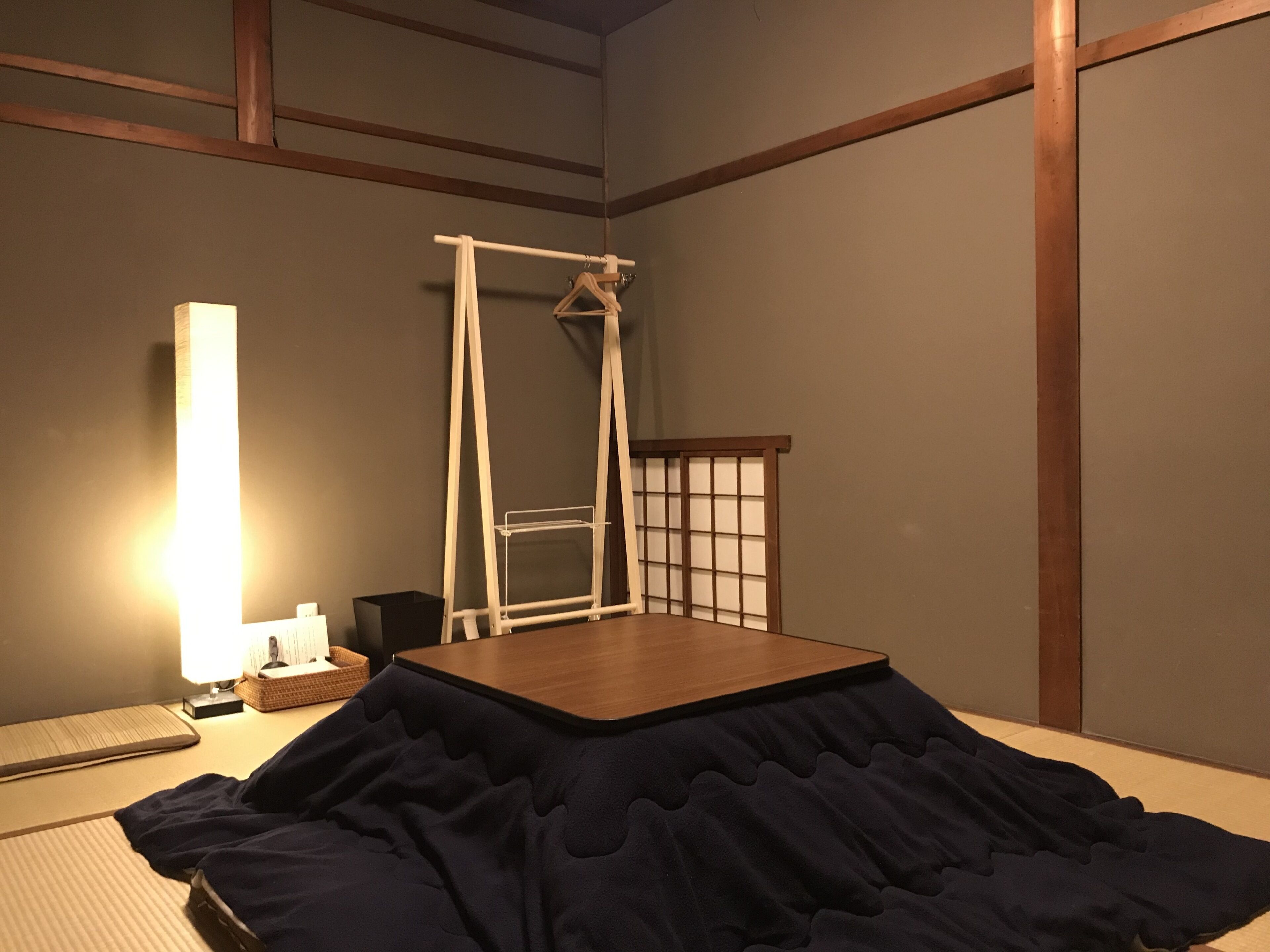A room with tatami flooring, a wooden table, a hanging shelf, and a traditional Japanese-style bed.