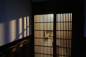 A room with a sliding shoji screen door, a wooden floor, and a dark wall. - HARUYA Naramachi - Hostel (Nara)