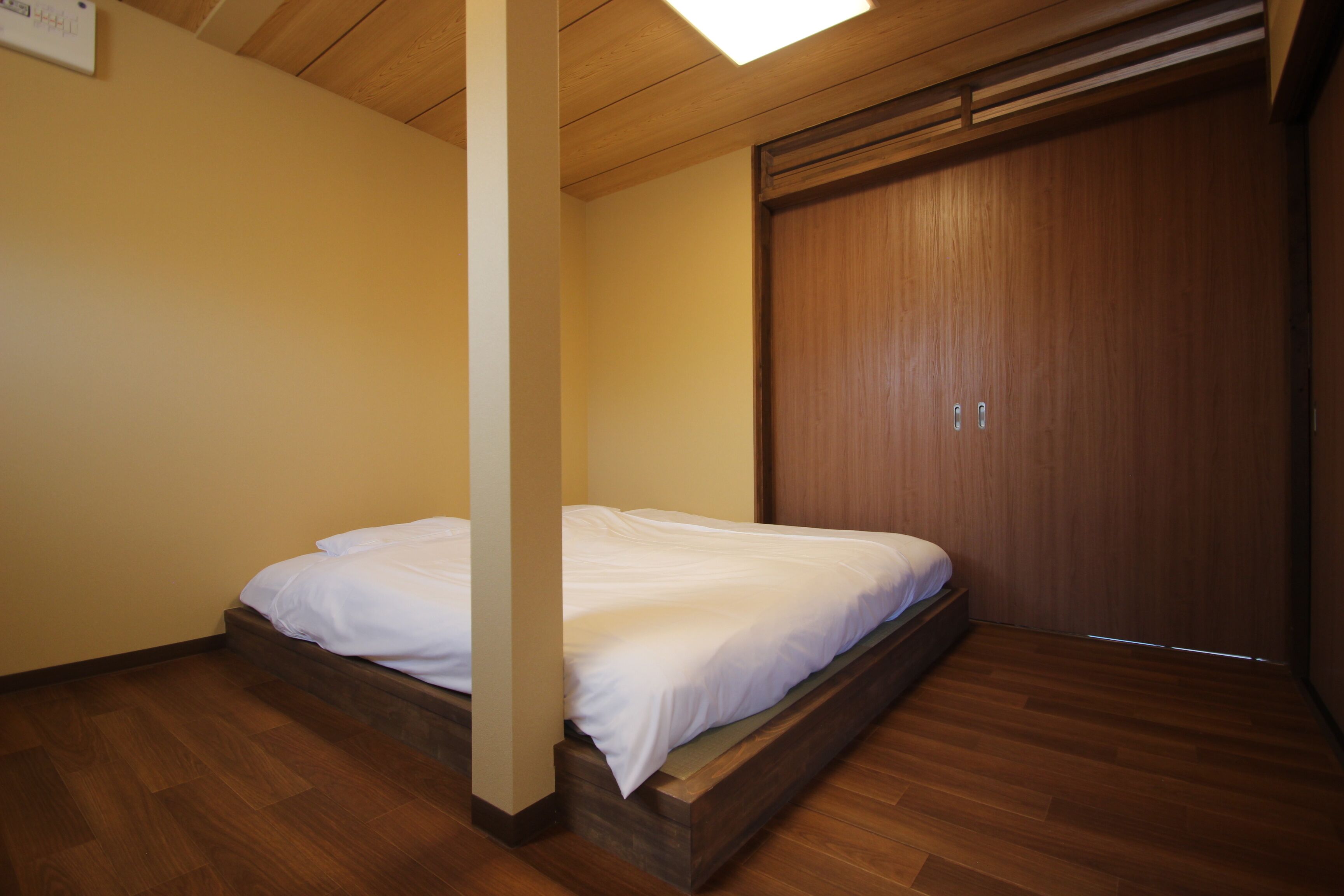 A bedroom with a wooden bed frame, a wooden wardrobe, and a wooden floor.