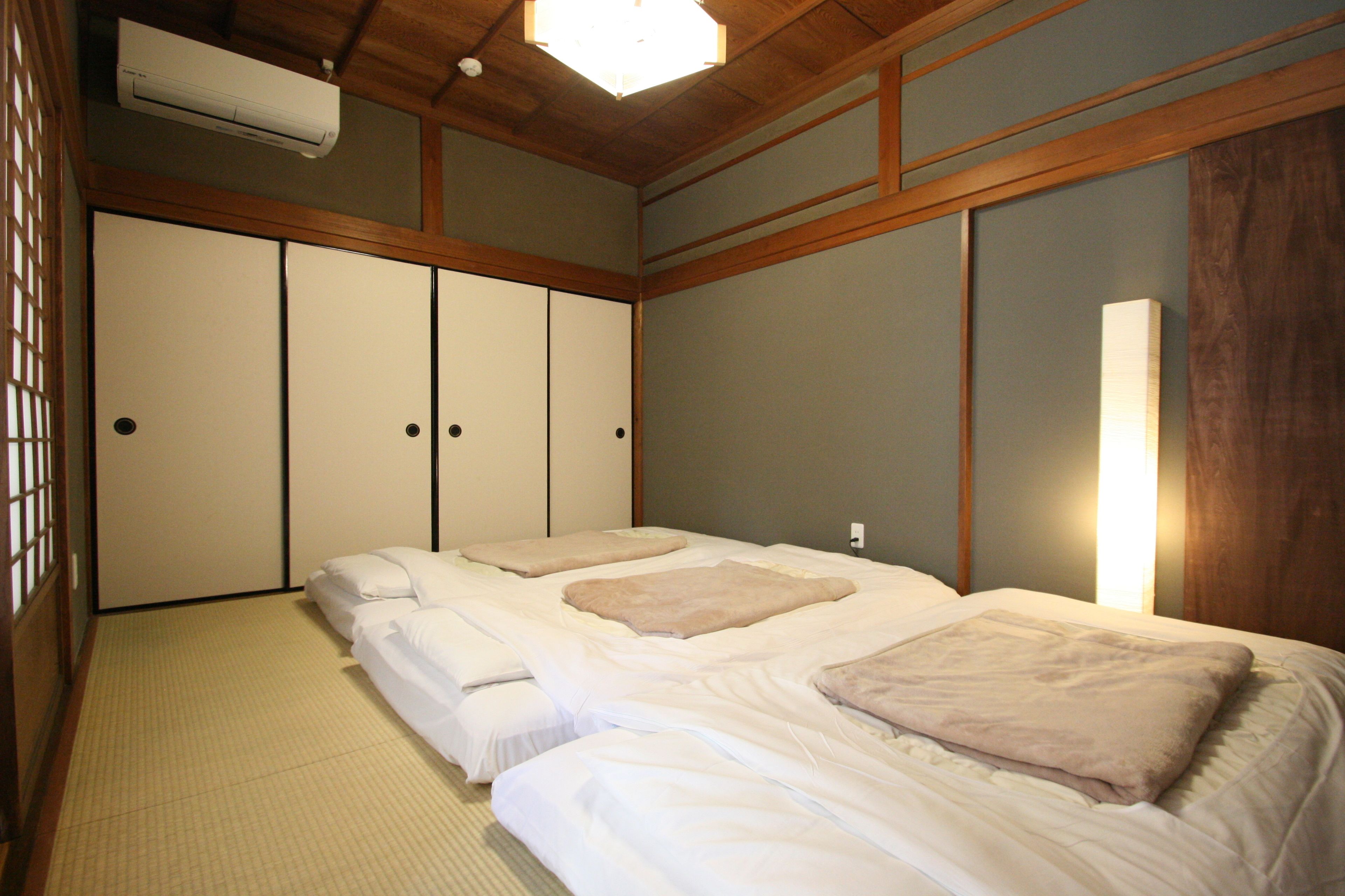 Una habitación tradicional japonesa con suelo de tatami, futón, puertas correderas y un ventilador de techo.