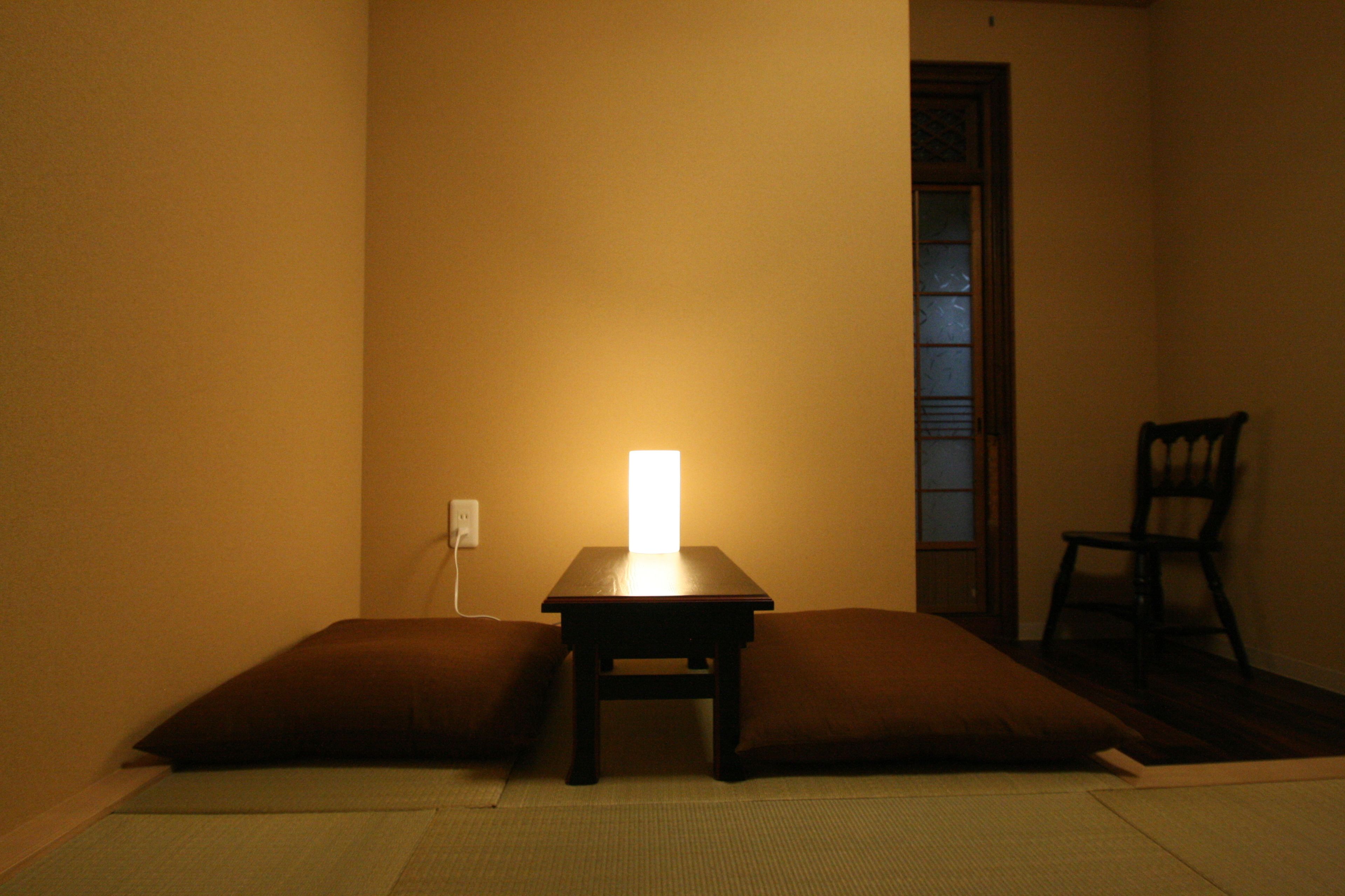 A room with a low table and two cushions, a chair, and a wall socket.