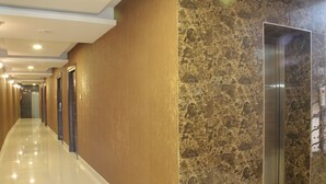 Un couloir d’hôtel avec un sol brillant, un mur de marbre et un ascenseur.